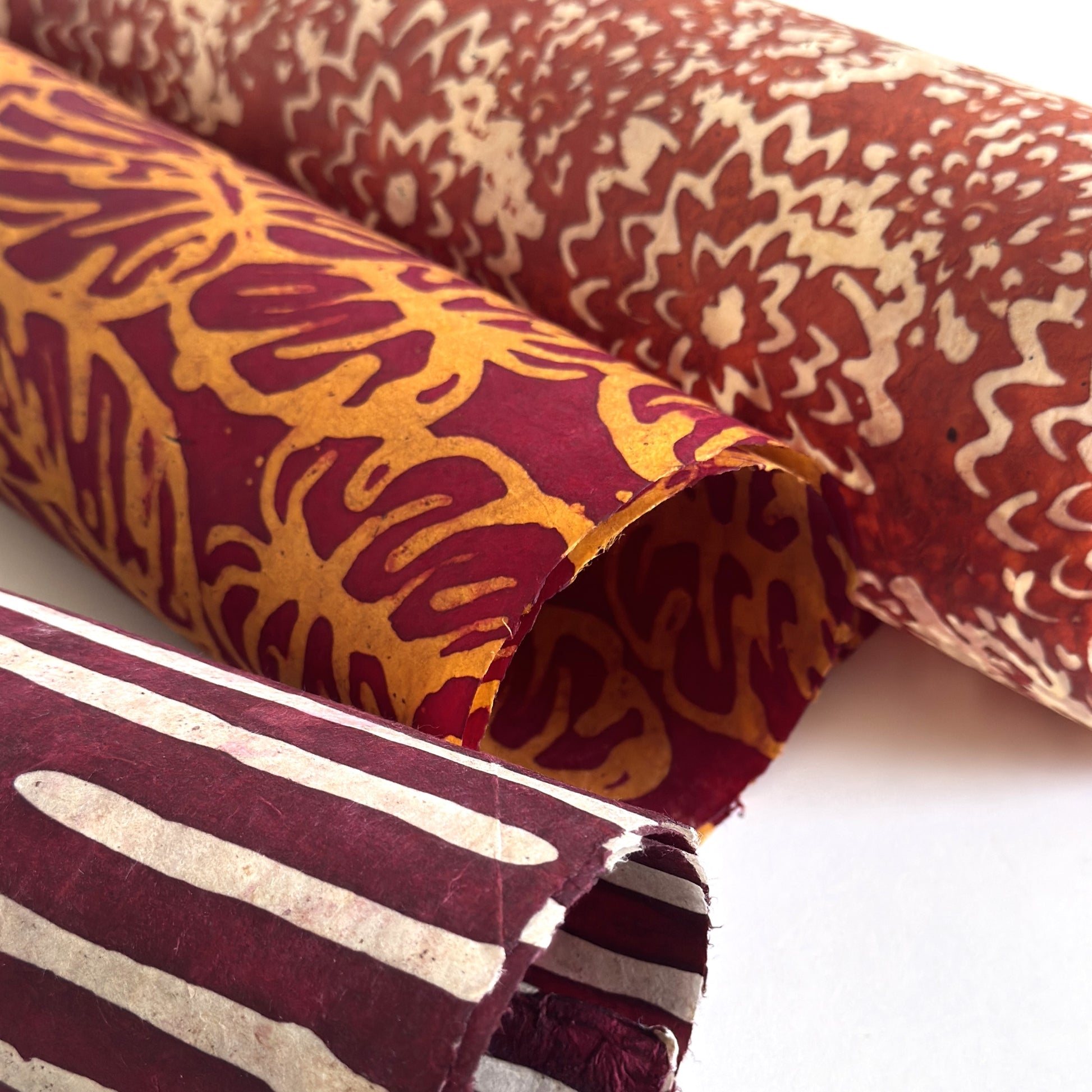 Nepalese handmade decorative lokta paper sheet with a leaf pattern in burgundy red and yellow.  Batik dyed using carved wooden blocks. Rolled with other batik designs