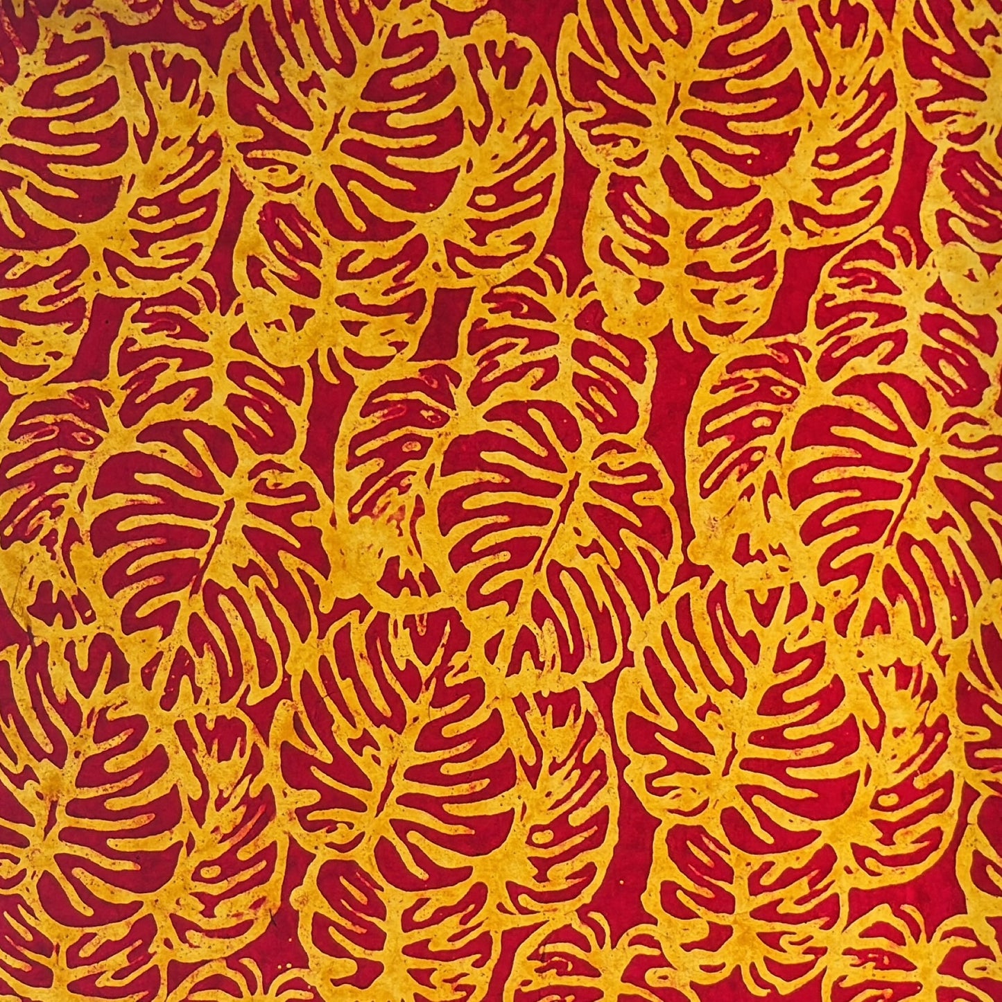 Nepalese handmade decorative lokta paper sheet with a leaf pattern in burgundy red and yellow.  Batik dyed using carved wooden blocks.  Photo taken next to the light to show the translucent nature.