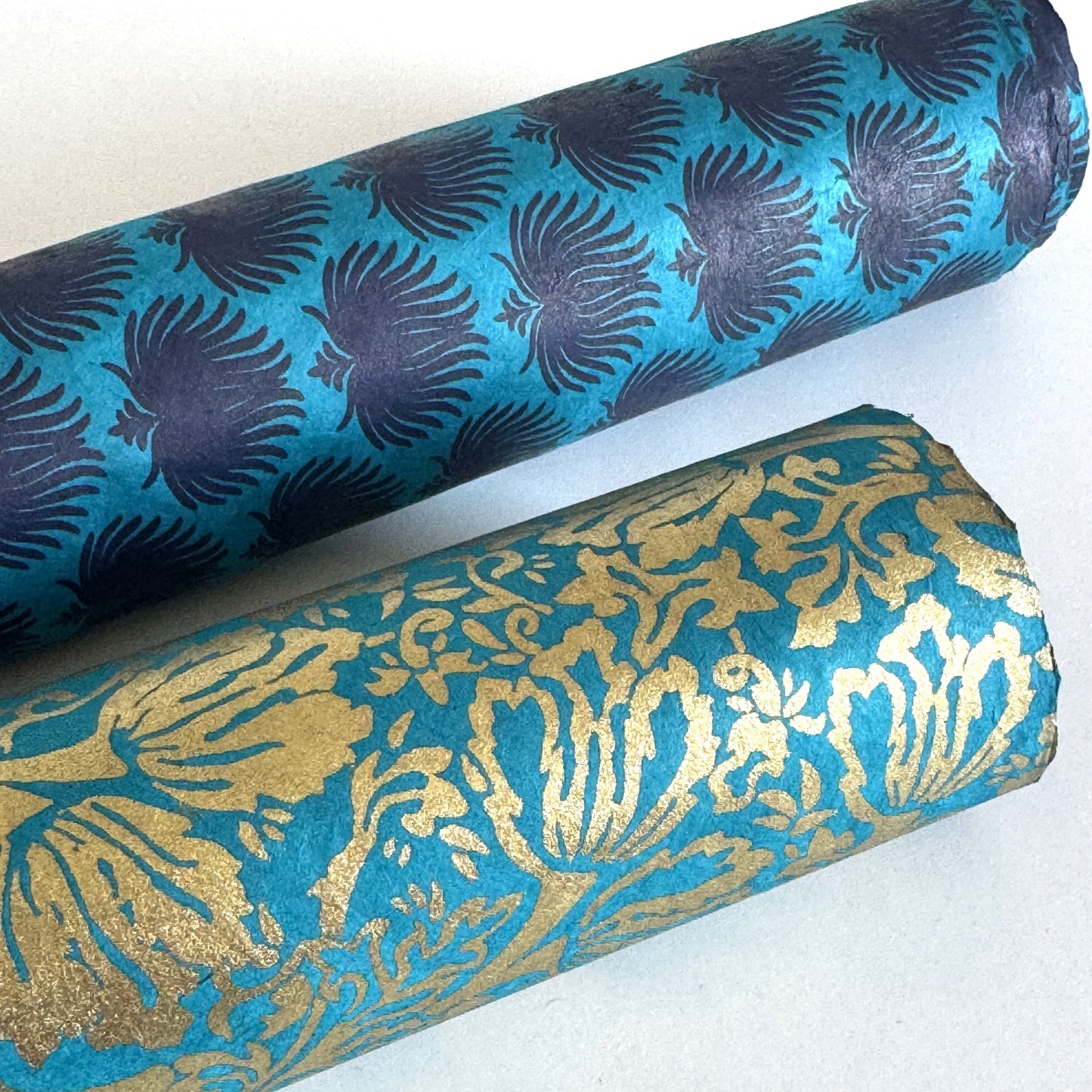 Nepalese handmade decorative lokta paper sheet with an inky blue palm leaf design screen printed on a teal lokta paper. Pictured rolled
