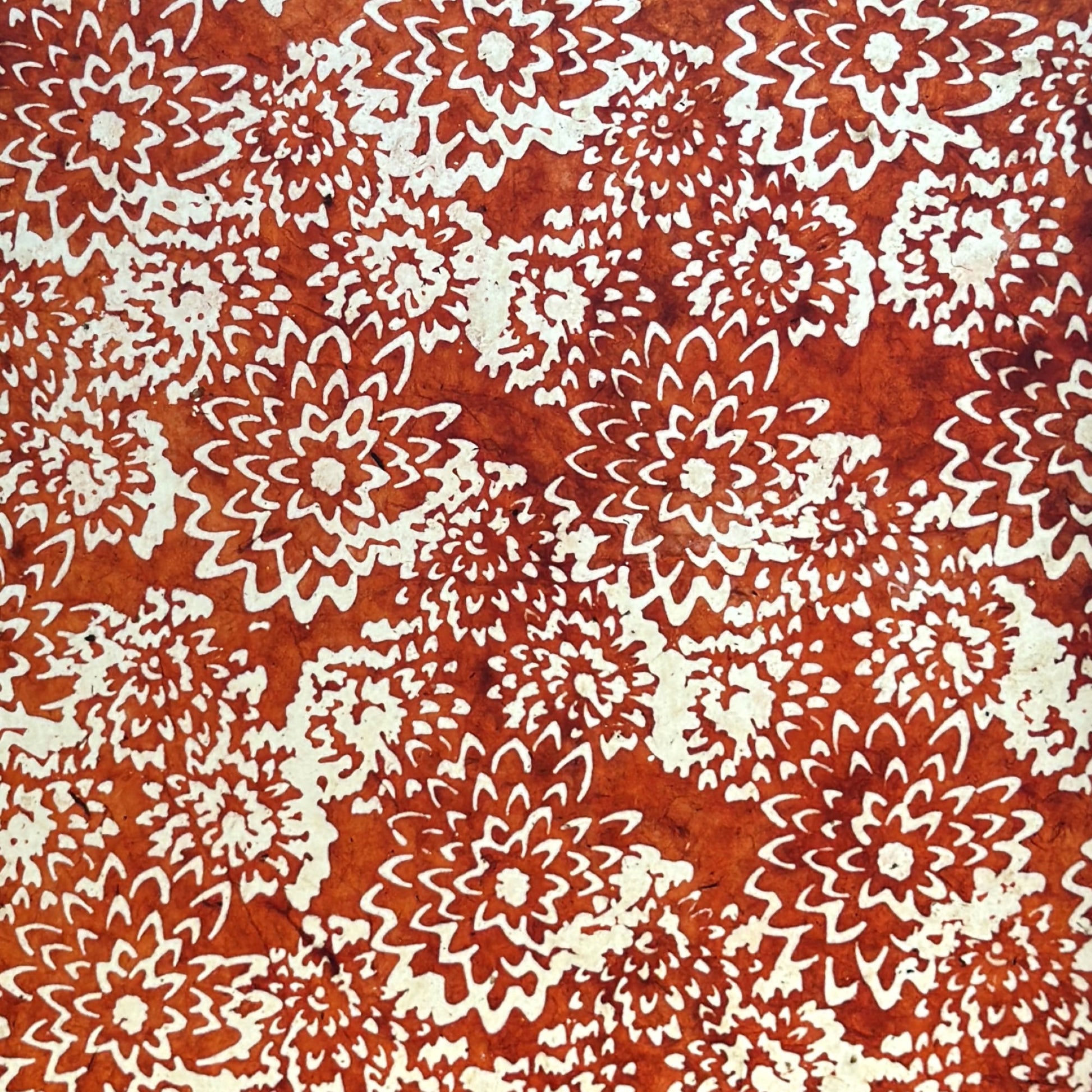 Nepalese handmade decorative lokta paper sheet with a floral pattern in rust and cream.  Batik dyed using carved wooden blocks.  Photographed next to the light to show translucent nature.
