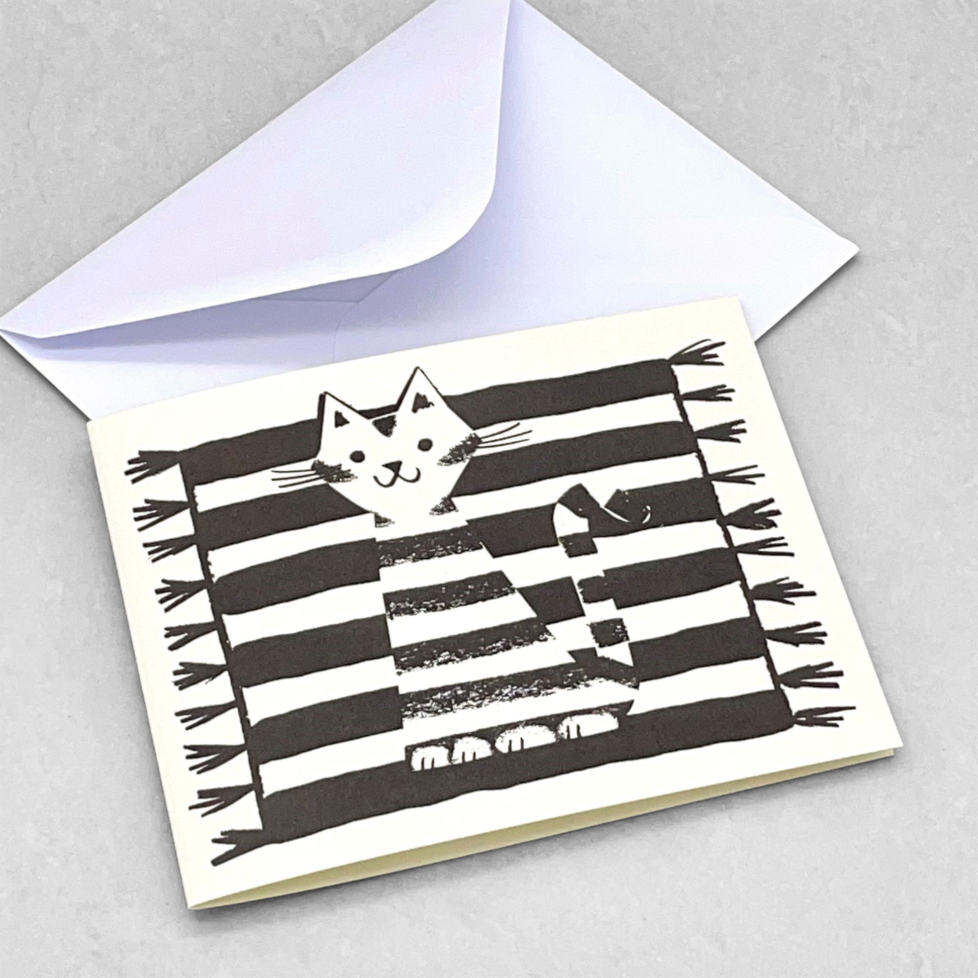 Small greeting card of a black and white stripy cat sitting on a black and white stripy rug by Lisa Jones Studio