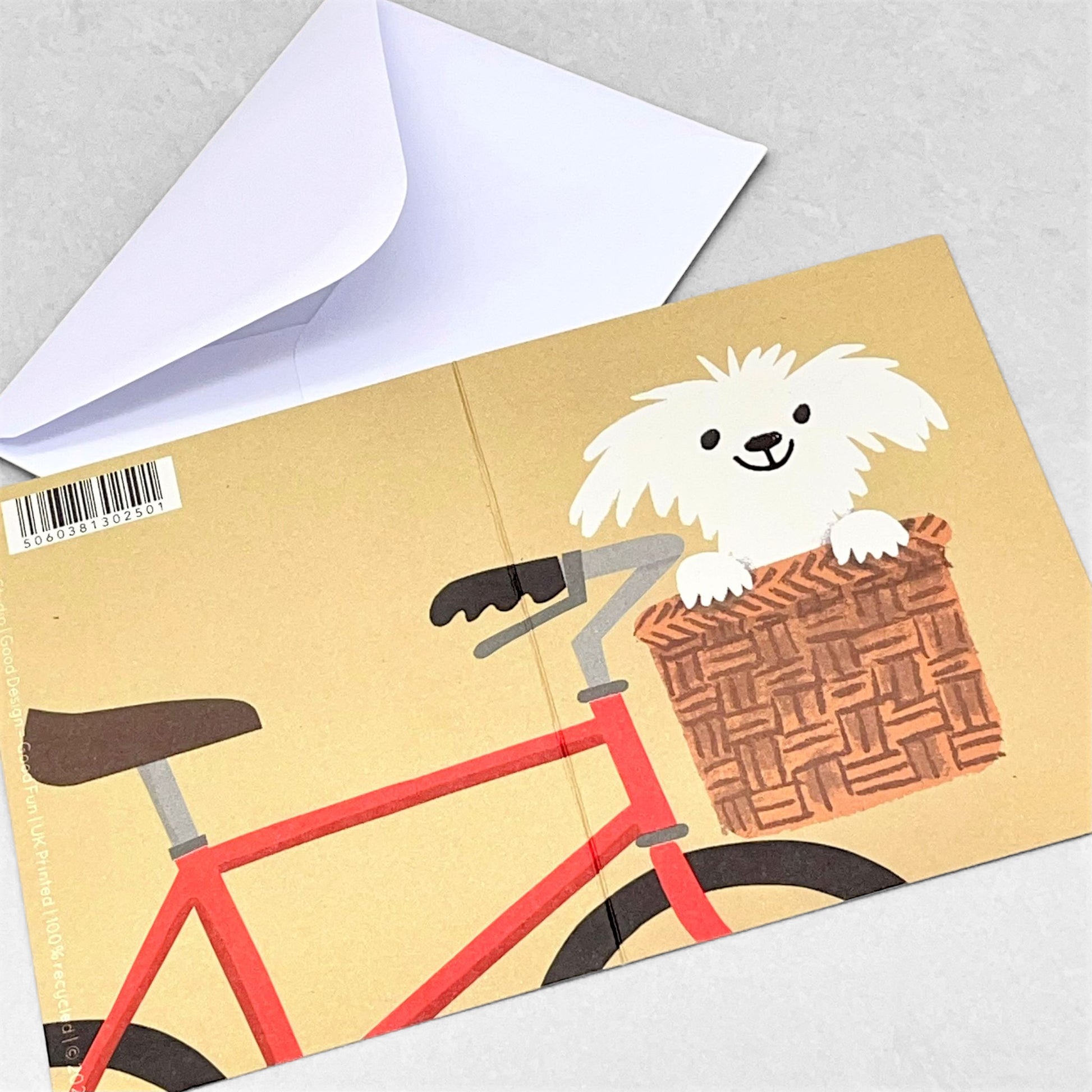 Small greetings card with a drawing of a happy white dog in the basket of a red bike, with beige backdrop by Lisa jones Studio