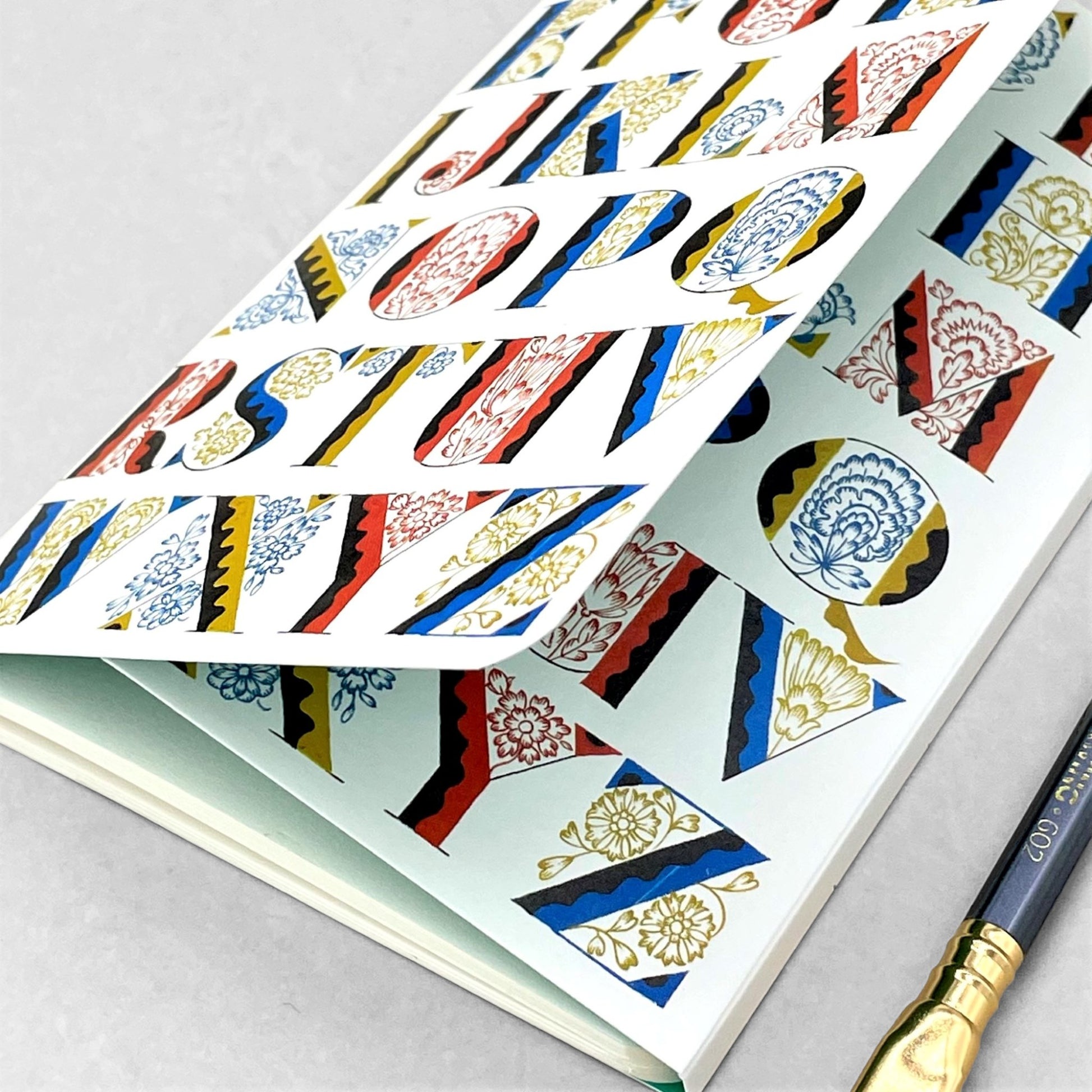 Small stitched notebook with a colourful alphabet cover design in red, blue and yellow on white background