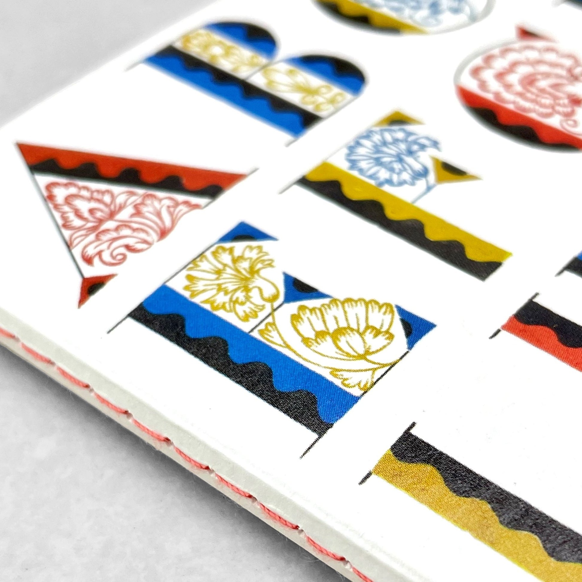 Small stitched notebook with a colourful alphabet cover design in red, blue and yellow on white background