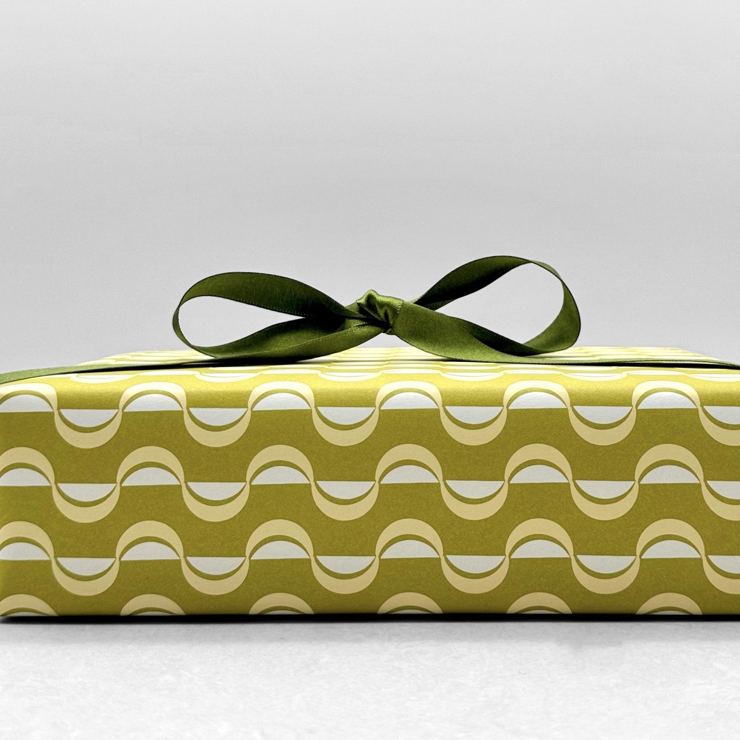 wrapping paper by ola studio with a wavy stripe design in chartreuse and lemon. Pictured wrapped with a green satin ribbon