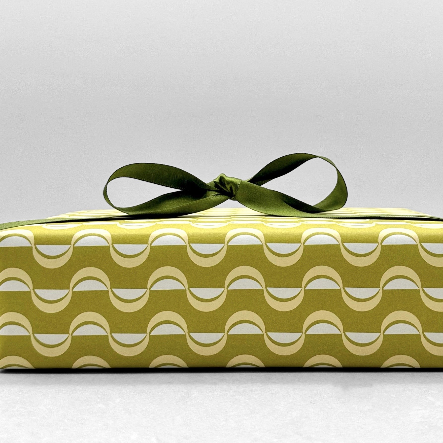 wrapping paper by ola studio with a wavy stripe design in chartreuse and lemon. Pictured wrapped with a green satin ribbon