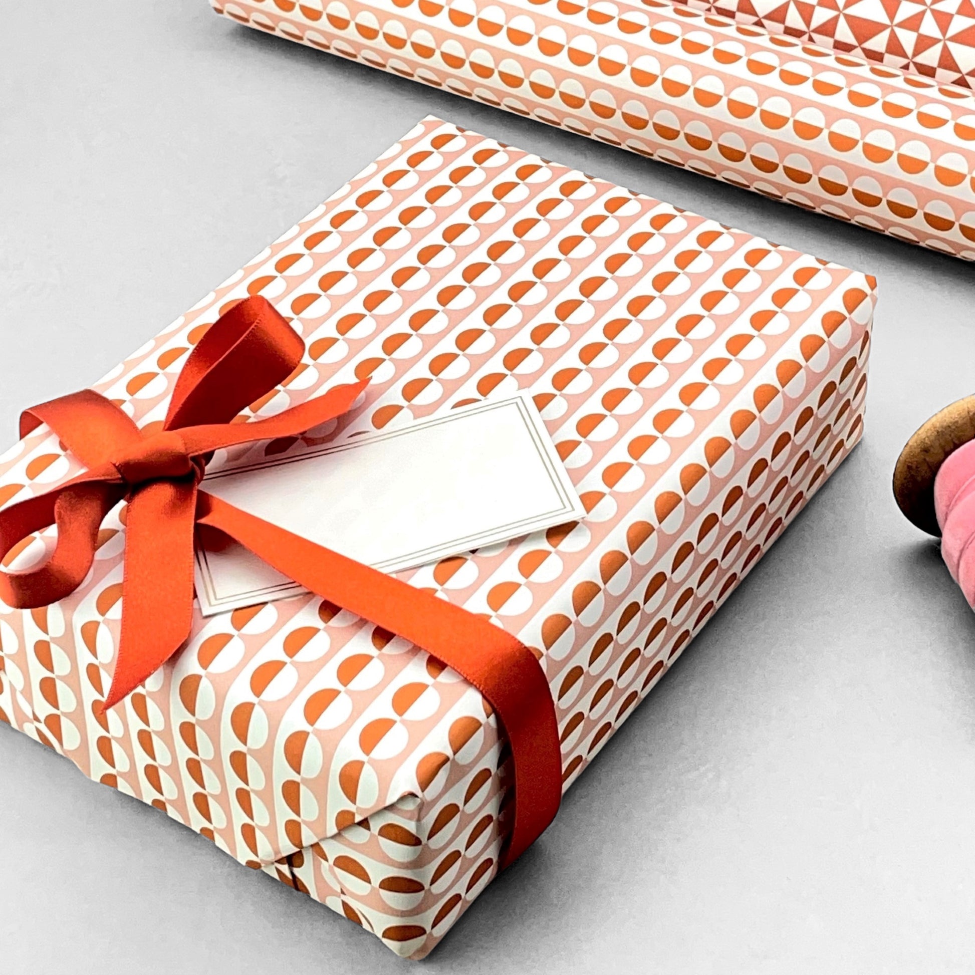 wrapping paper with an abstract circle pattern in orange and pale pink by Ola Studio