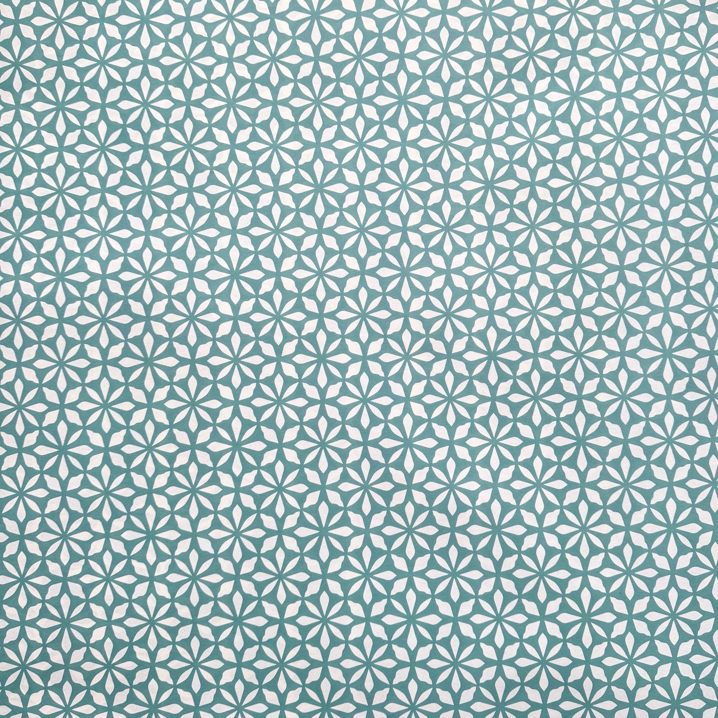 wrapping paper by Otto Editions with a cut-out flower design in white on an aqua blue background.