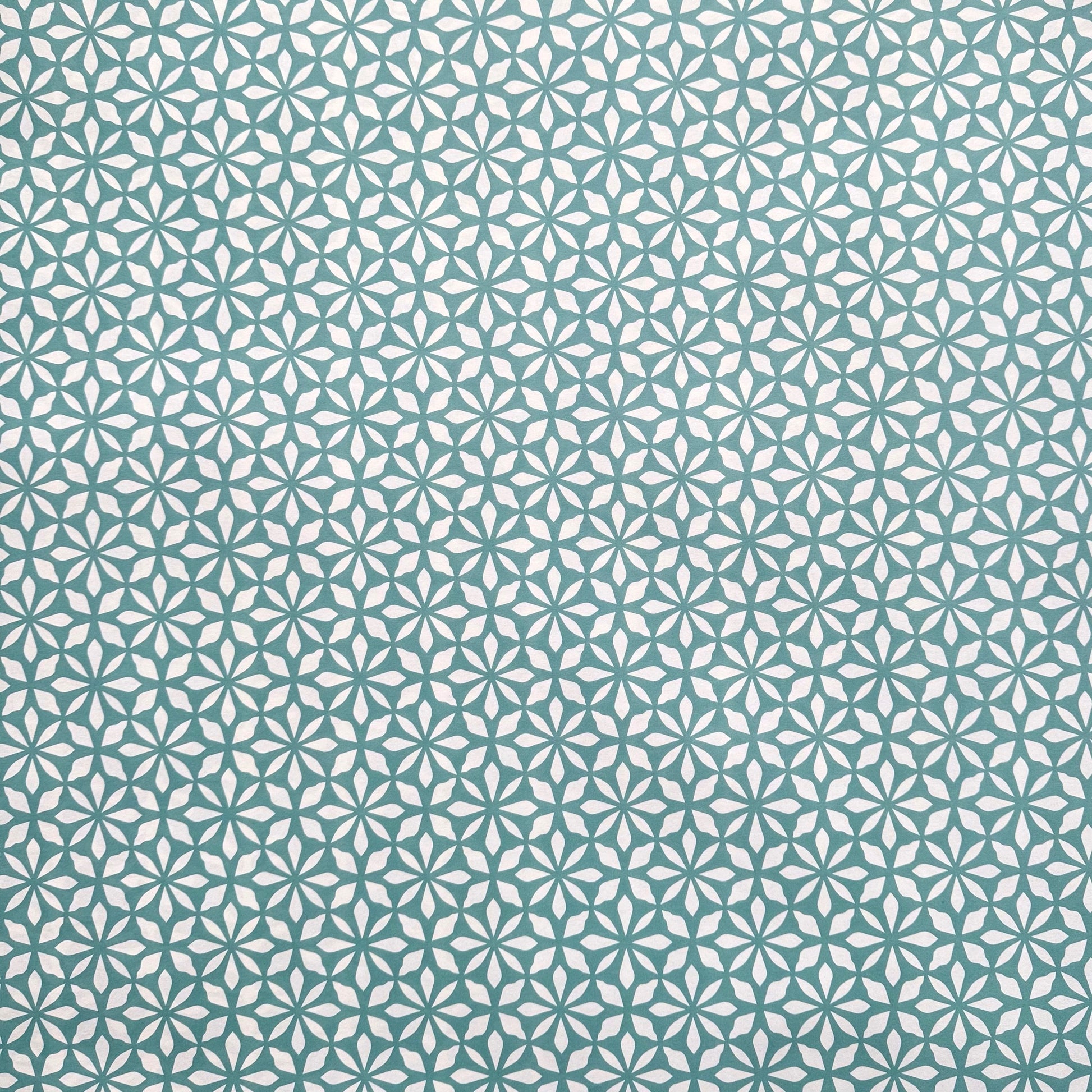 wrapping paper by Otto Editions with a cut-out flower design in white on an aqua blue background.