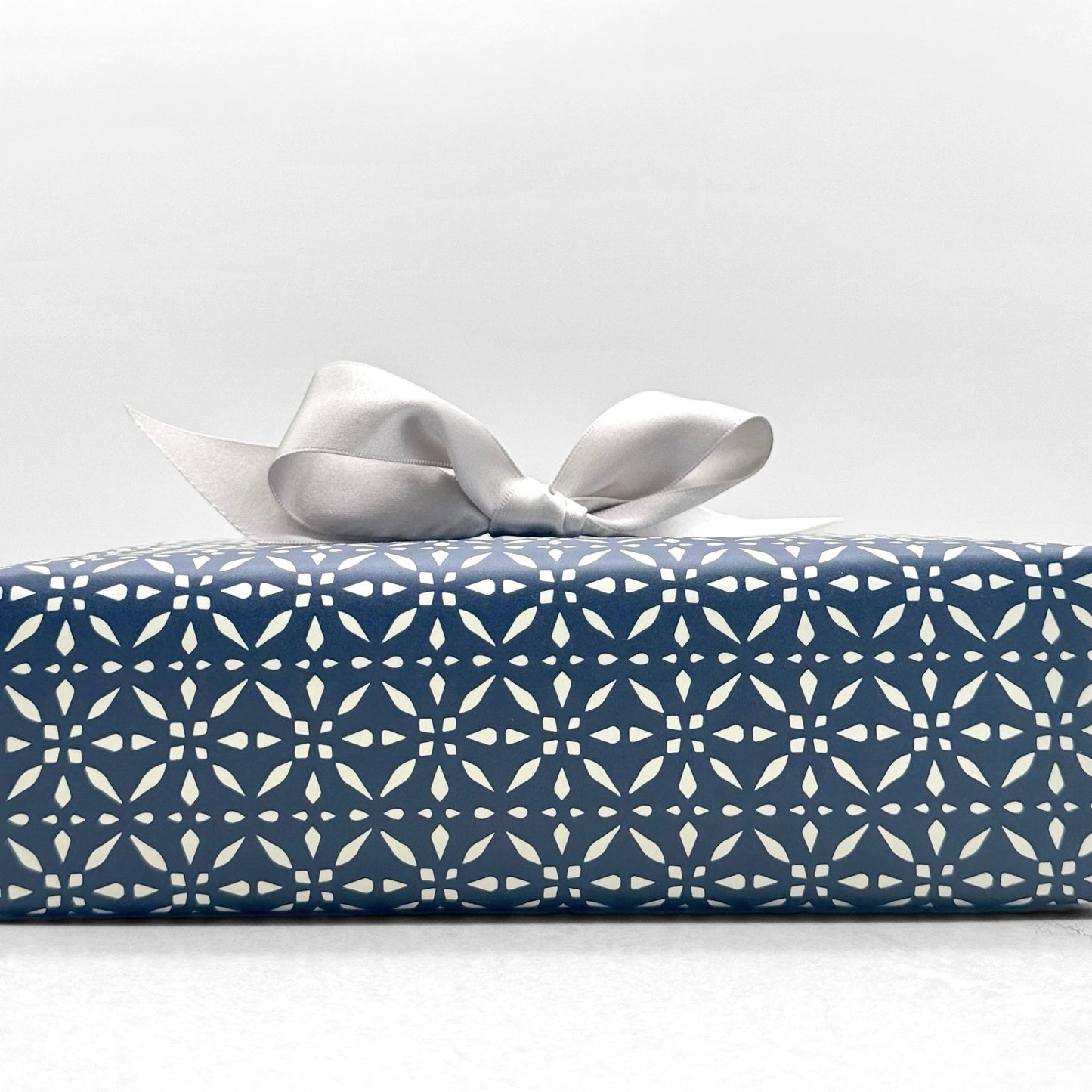 wrapping paper by Otto Editions with a cut-out design in white on an indigo blue background. Pictured wrapped as a present with a silver bow