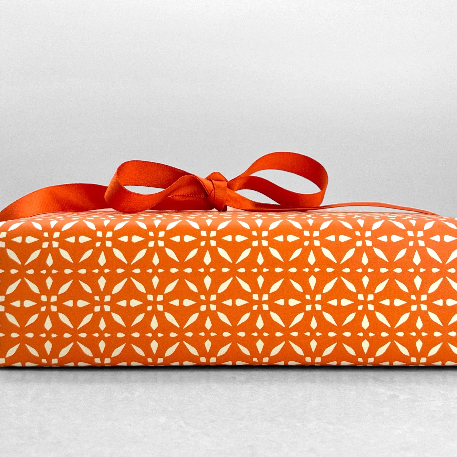 wrapping paper by Otto Editions with a cut-out design in white on a spice orange background. Pictured wrapped as a present with a bow