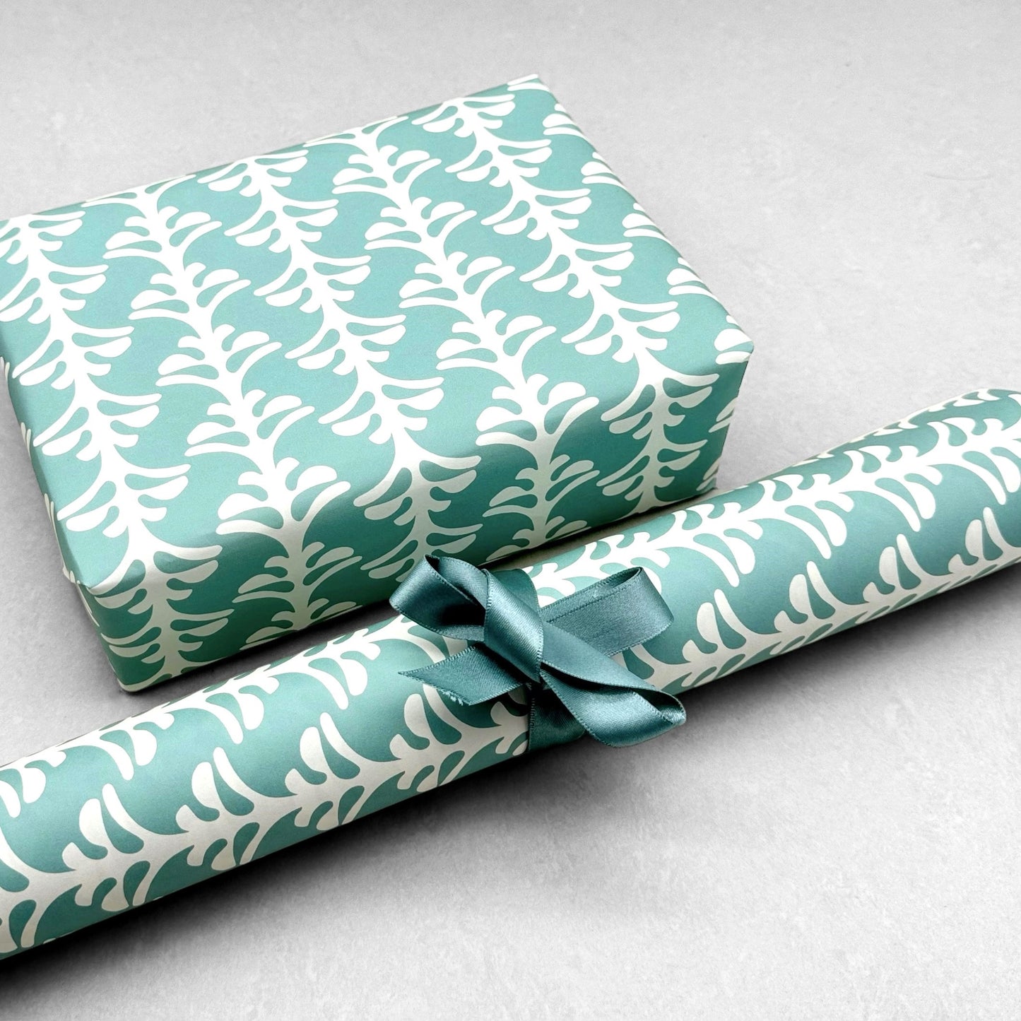 wrapping paper by Otto Editions with a cut-out palm design in white on an aqua blue background. Pictured wrapped as a present with a roll of the paper