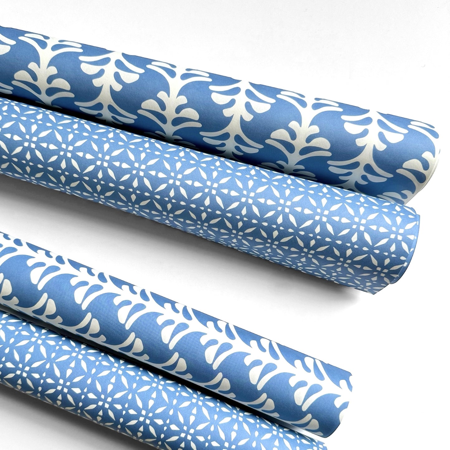 wrapping paper by Otto Editions with a cut-out palm design in white on a sky blue background. Pictured rolled with other designs