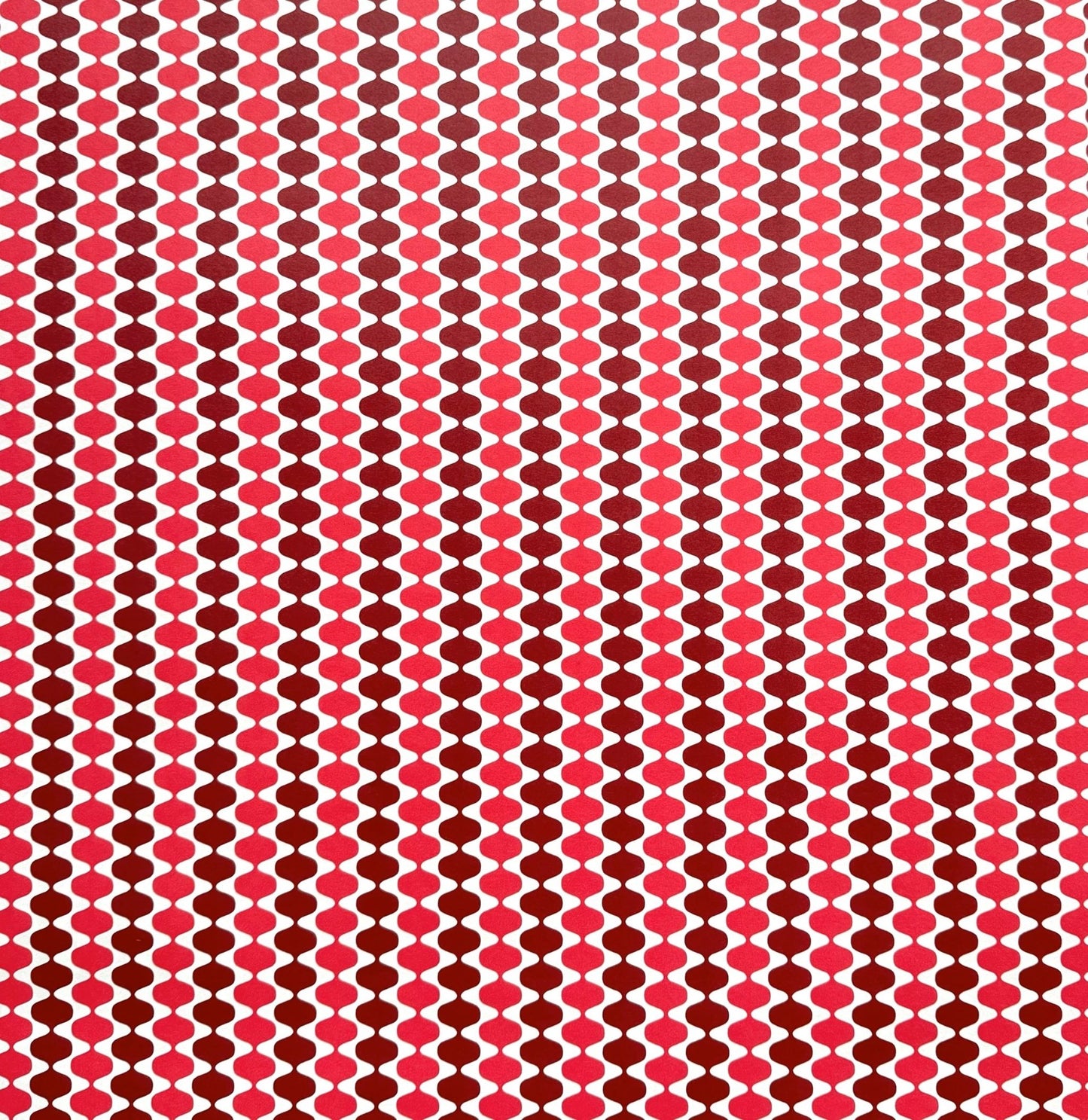wrapping paper by Otto Editions with a cut-out wavy design in white on a pink and burgundy background.