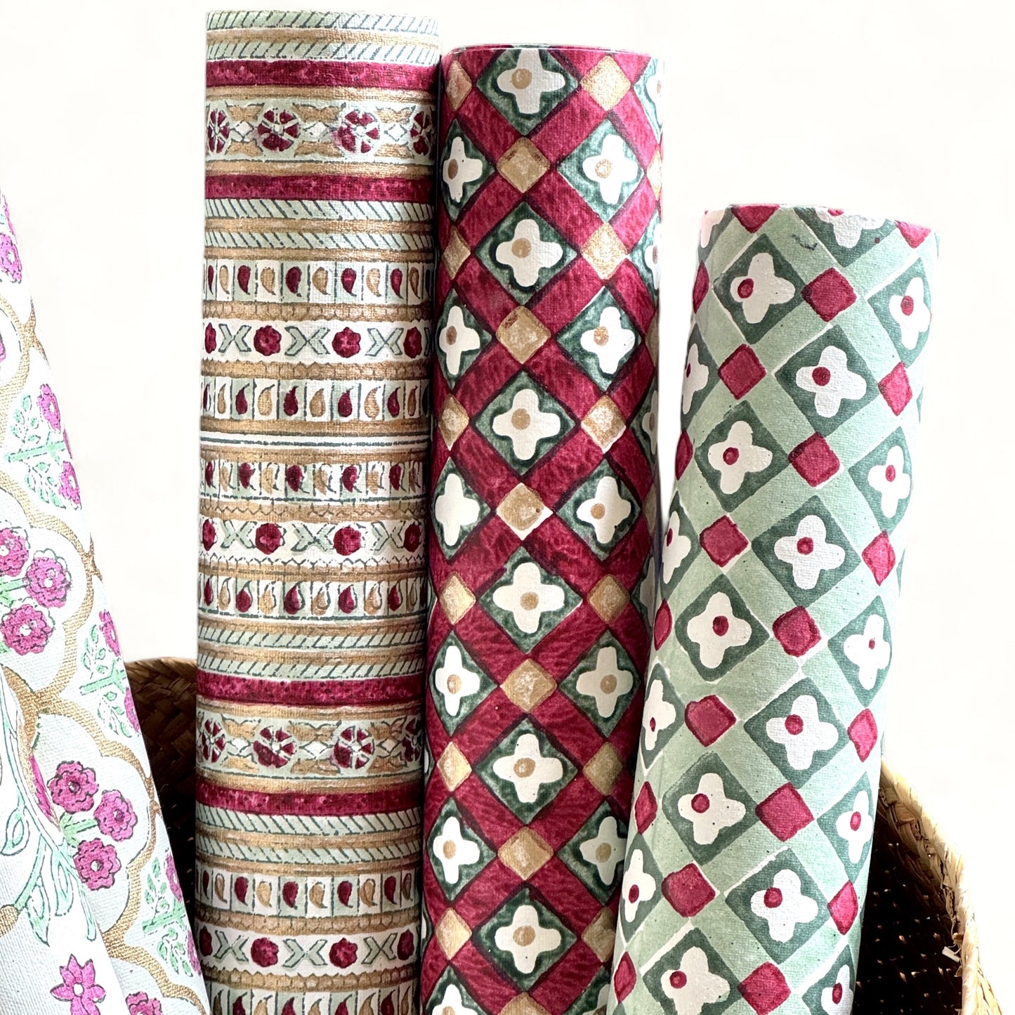 Hand block printed wrapping paper with a floral checked pattern in red, green and gold. Pictured rolled alongside other designs