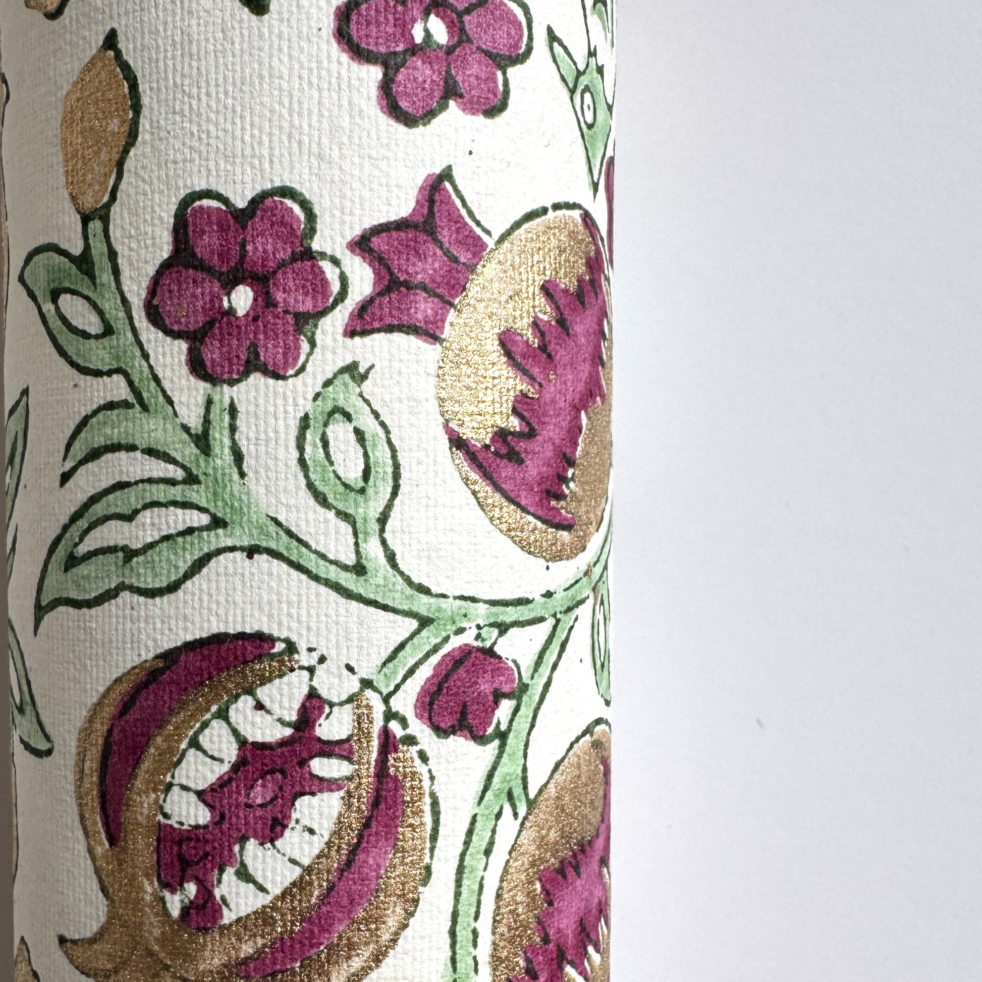 Hand block printed wrapping paper with a pattern of pomegranates in cherry red, green and gold. Detail of the pomegranate