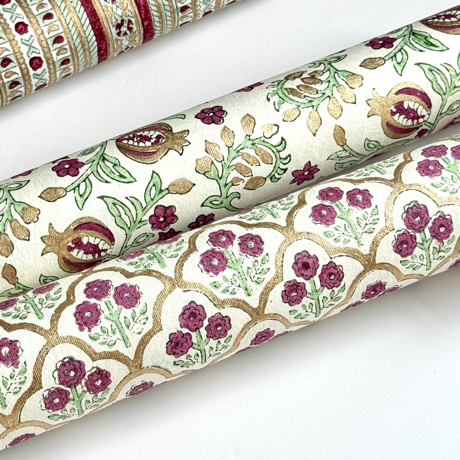 Hand block printed wrapping paper with a trellis pattern with flowers in cherry red, green and gold. Rolled alongside another design