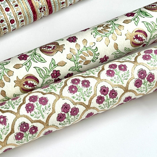 Hand block printed wrapping paper with a trellis pattern with flowers in cherry red, green and gold. Rolled alongside another design