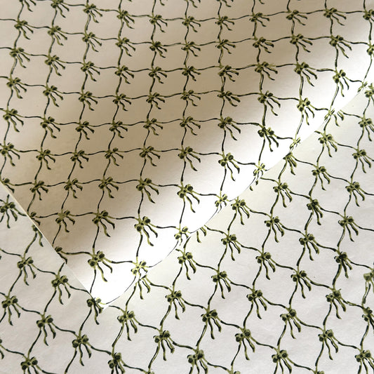 a sheet of hand block printed paper with a pattern of green bows on white