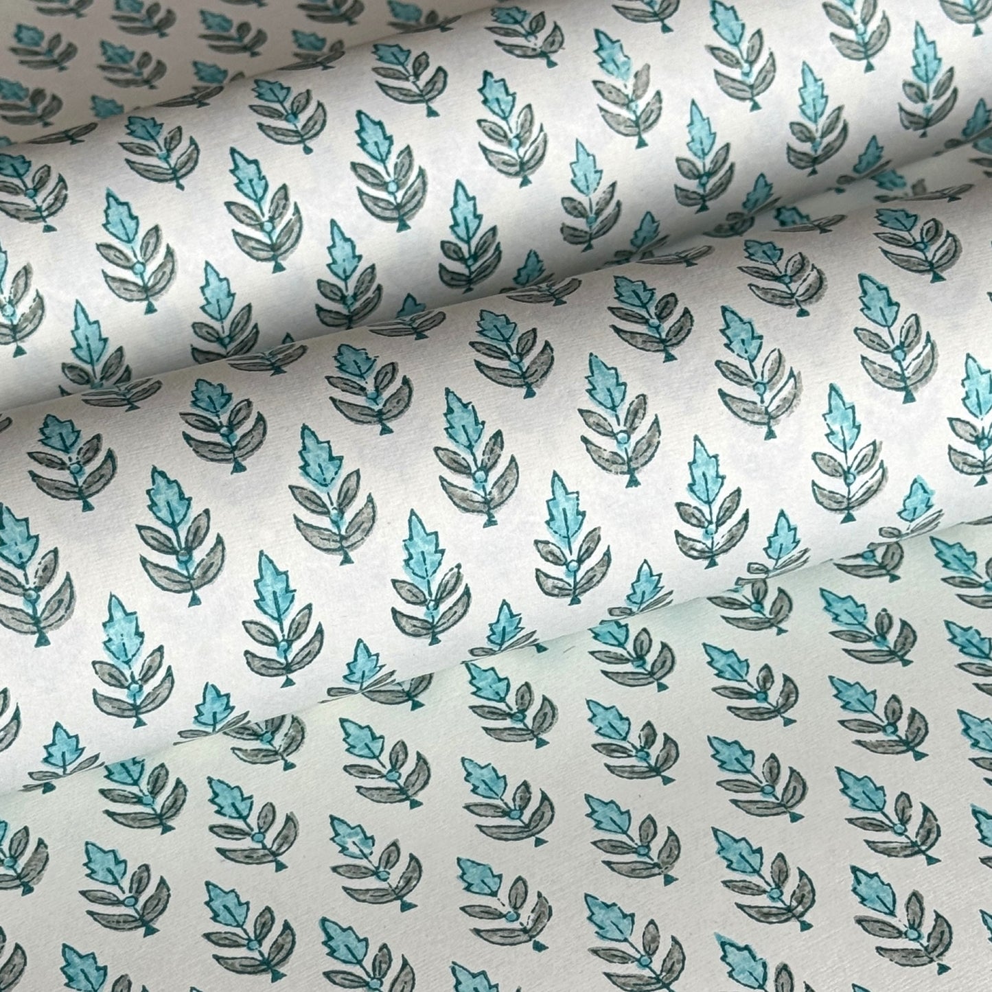 hand block printed wrapping paper by paper mirchi with a repeat floral pattern in turquoise and soft green on white backdrop. close up