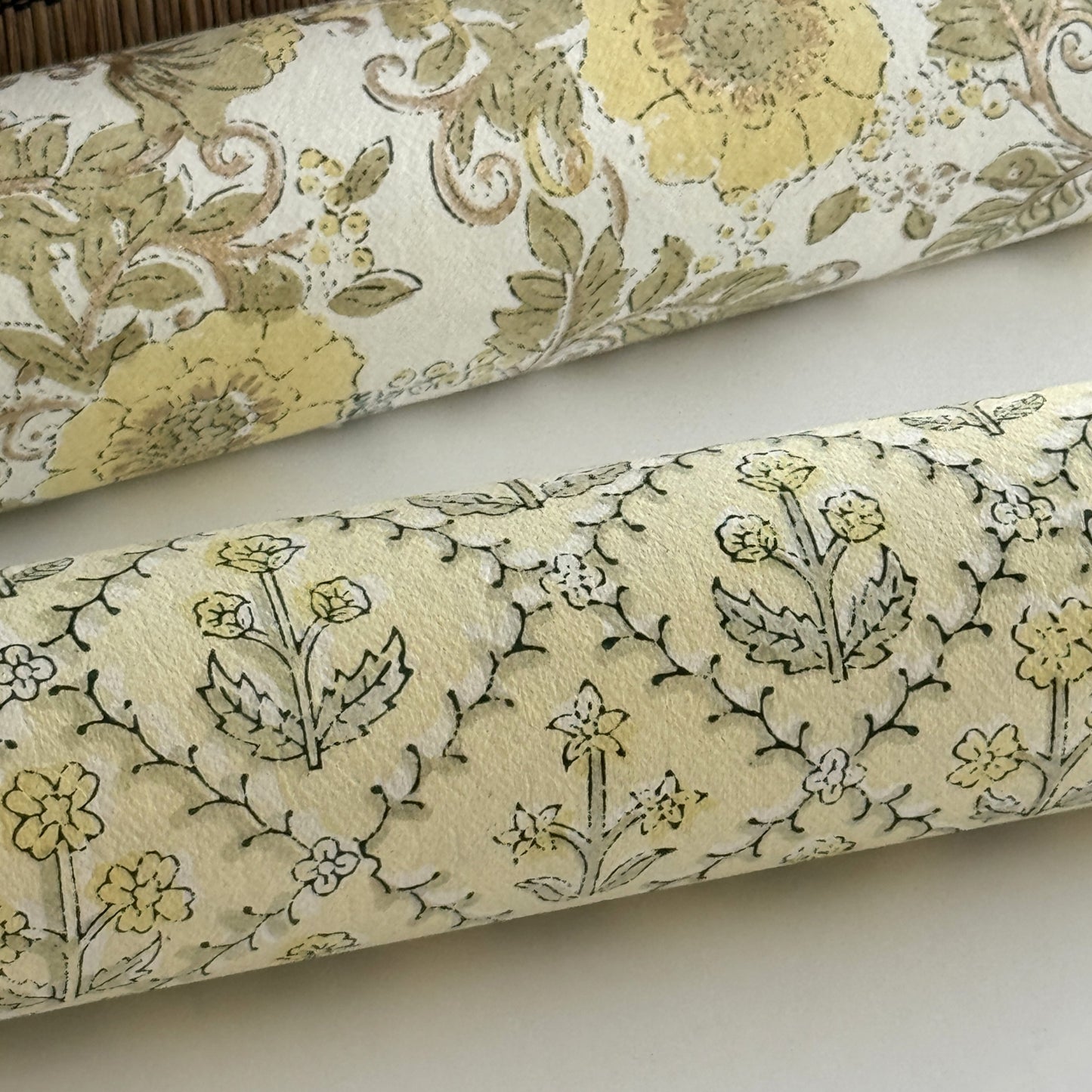 a sheet of hand block printed wrapping paper with a floral lattice design in soft buttermilk yellow. close up of the paper rolled