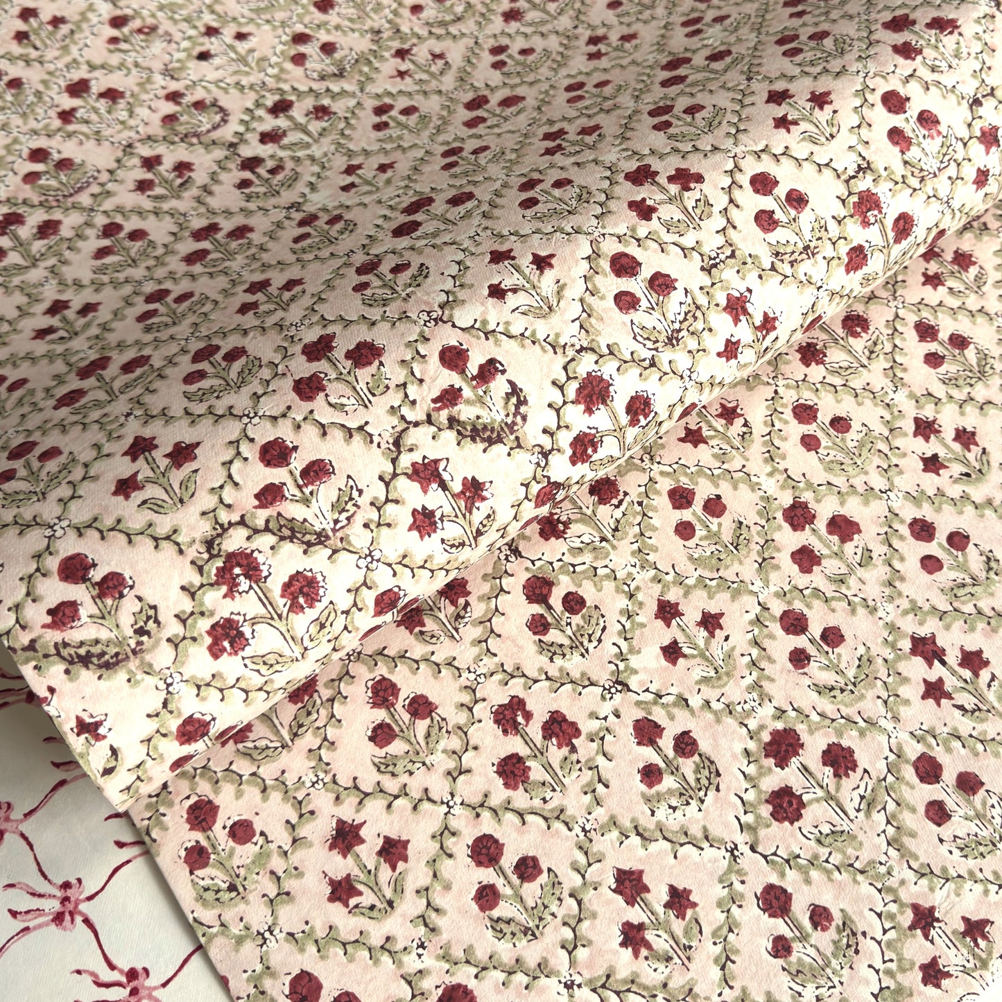 a sheet of hand block printed paper with a floral trellis design in blush pink, sage green and deep red