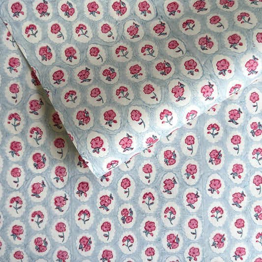 a sheet of hand block printed wrapping paper with a ditsy floral pattern of pink flowers in white ovals with a soft blue backdrop
