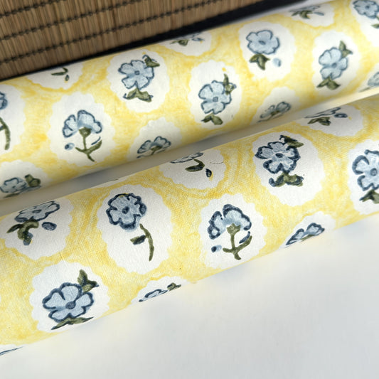 a sheet of hand block printed wrapping paper with a ditsy floral pattern of blue flowers in white ovals with a soft yellow backdrop