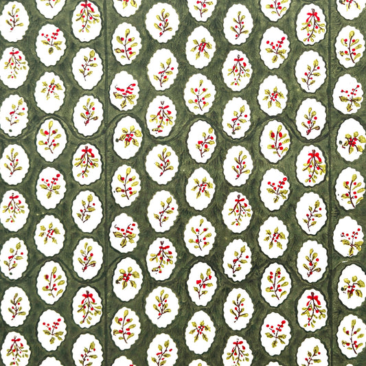 a sheet of block printed paper with a dark green backdrop and white oval scallops with winter foliage motif in the centre