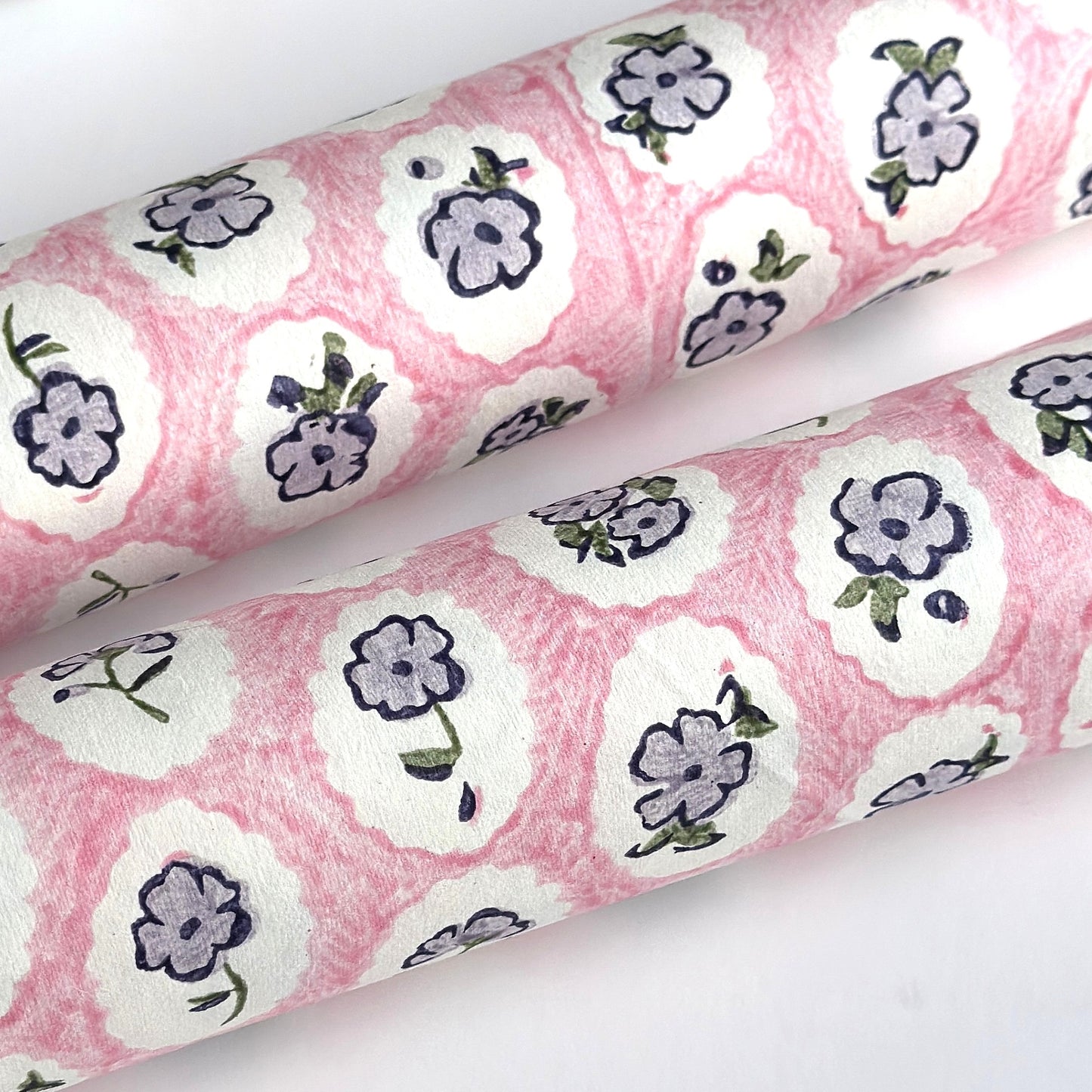 a sheet of hand block printed paper with a ditsy floral design, little violet flowers in a white oval with a pink background
