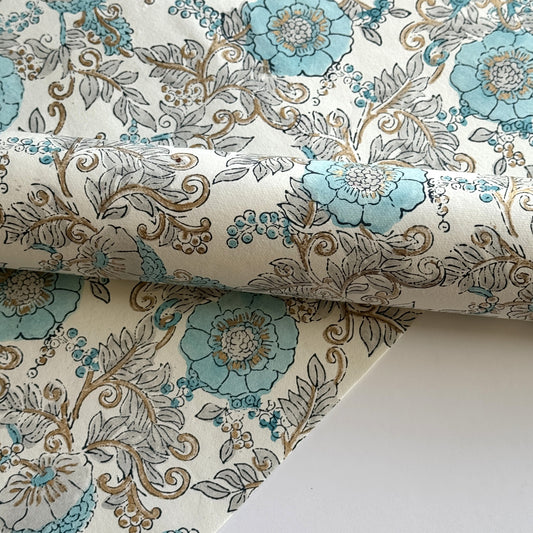 a sheet of hand block printed wrapping paper with a floral wild rose design in opal blue and gold
