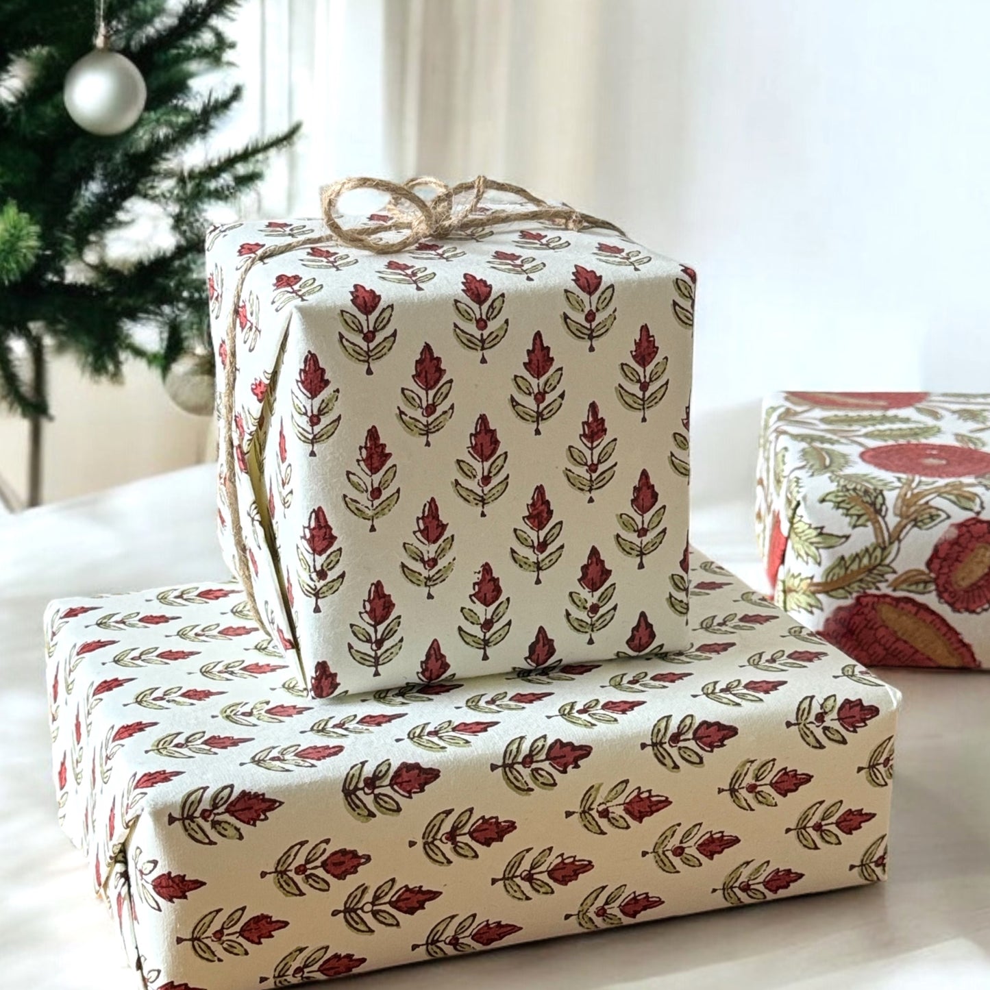 block printed paper by Paper Mirchi with a repeat block print pattern of a little stylised flower in dark burgundy and soft green on white backdrop, pictured wrapping two presents and tied with twine