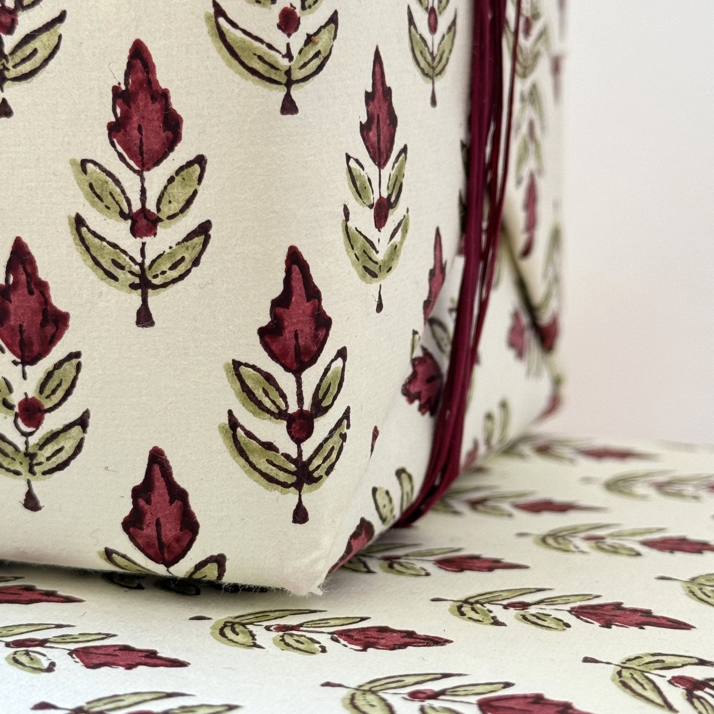 block printed paper by Paper Mirchi with a repeat block print pattern of a little stylised flower in dark burgundy and soft green on white backdrop. Close up