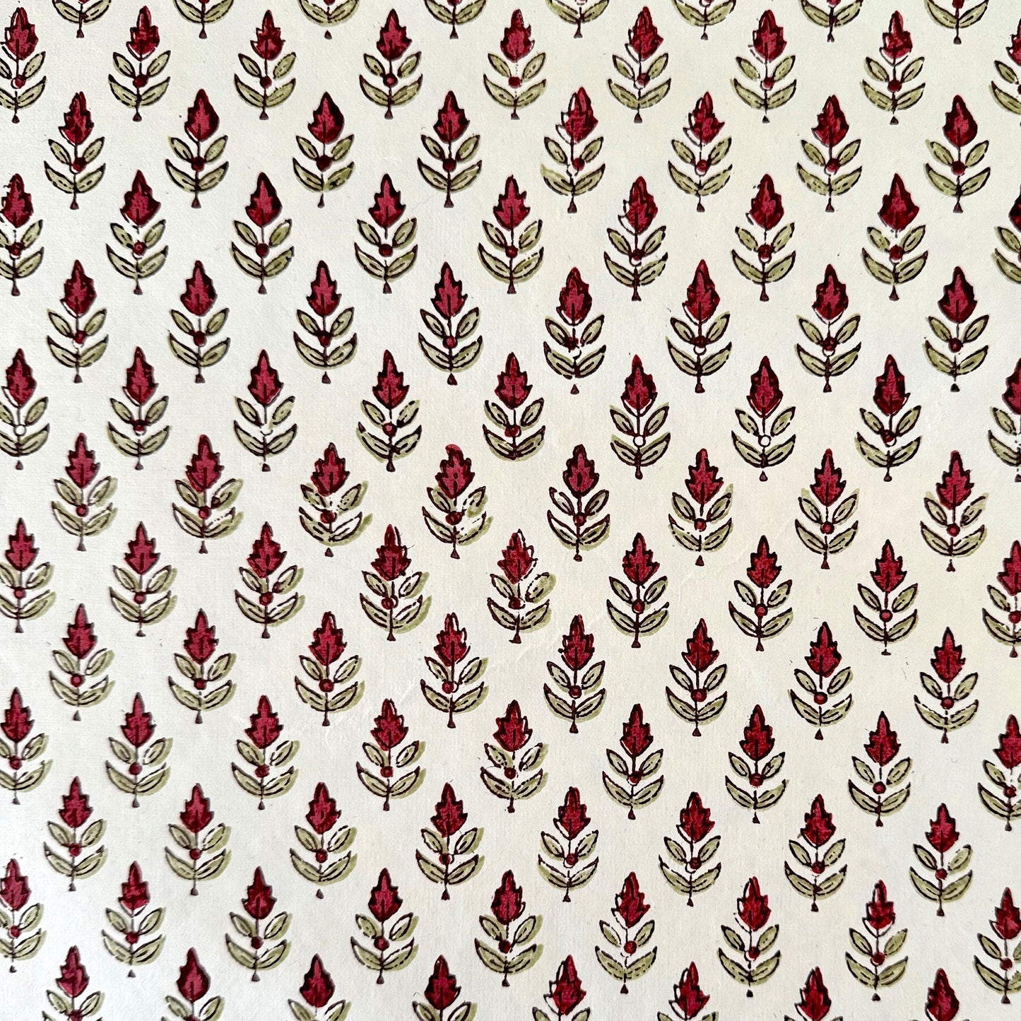 block printed paper by Paper Mirchi with a repeat block print pattern of a little stylised flower in dark burgundy and soft green on white backdrop.