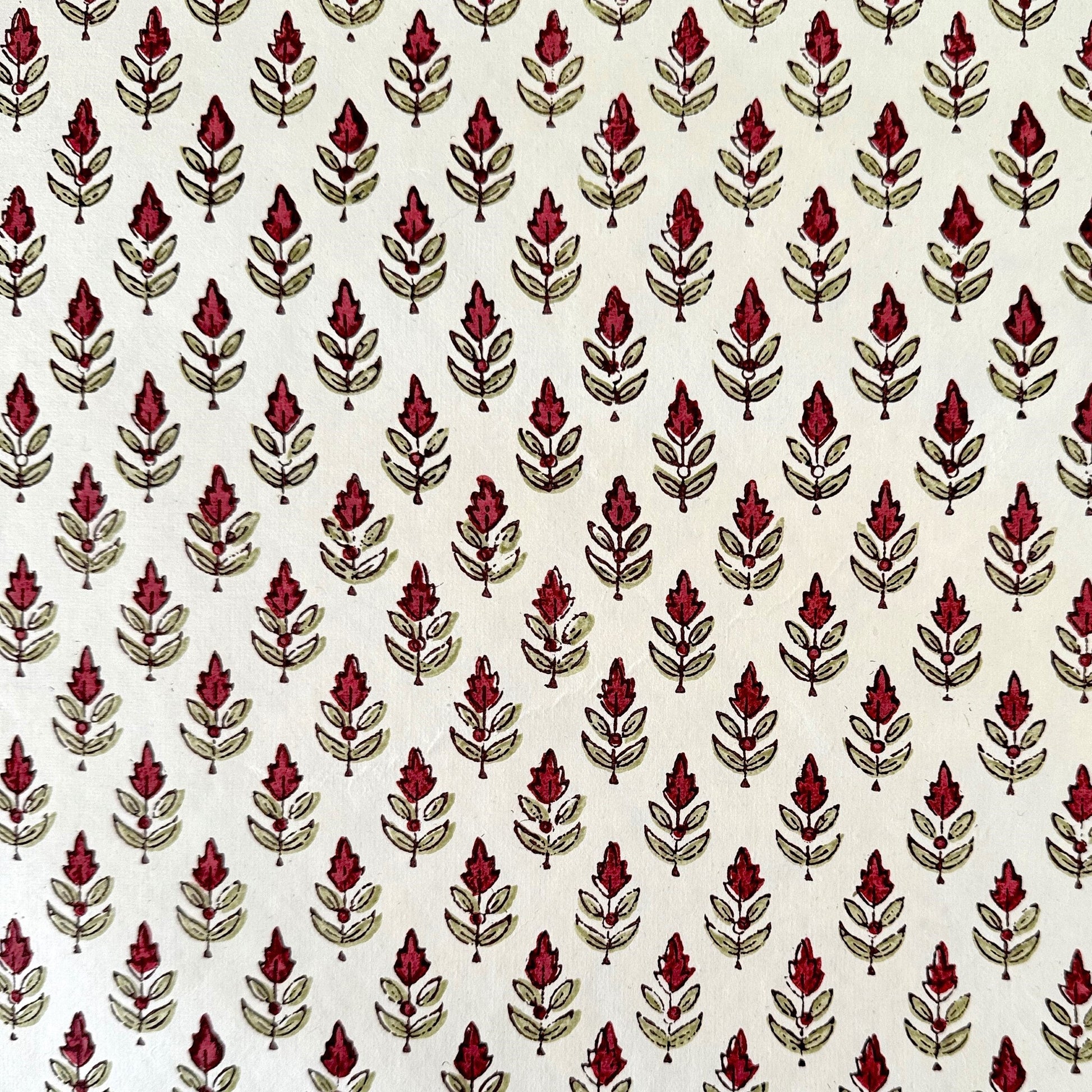 block printed paper by Paper Mirchi with a repeat block print pattern of a little stylised flower in dark burgundy and soft green on white backdrop.