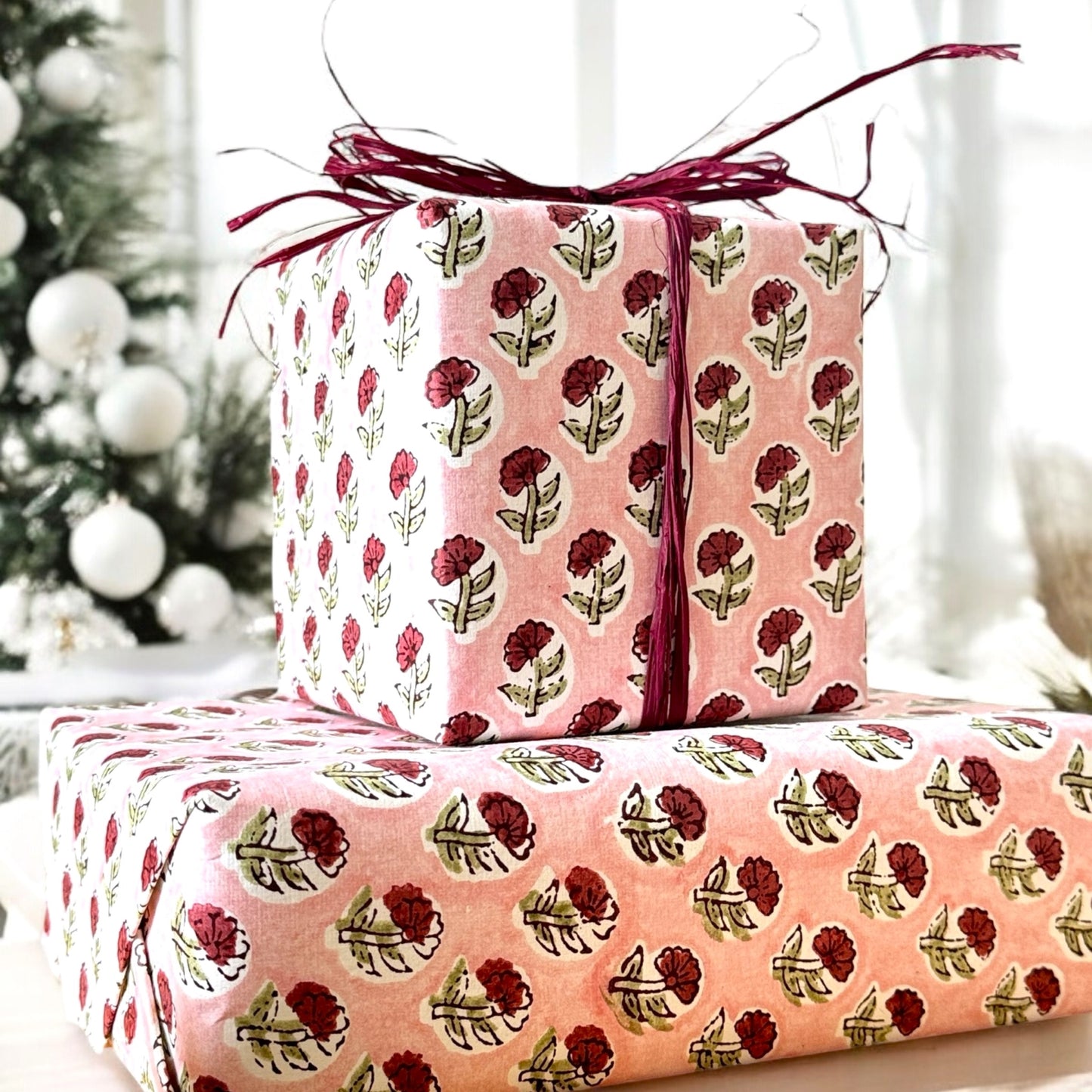 hand block printed patterned paper by Paper Mirchi, red daisy print on pink background, image shows two presents wrapped in the paper with a pink raffia ribbon