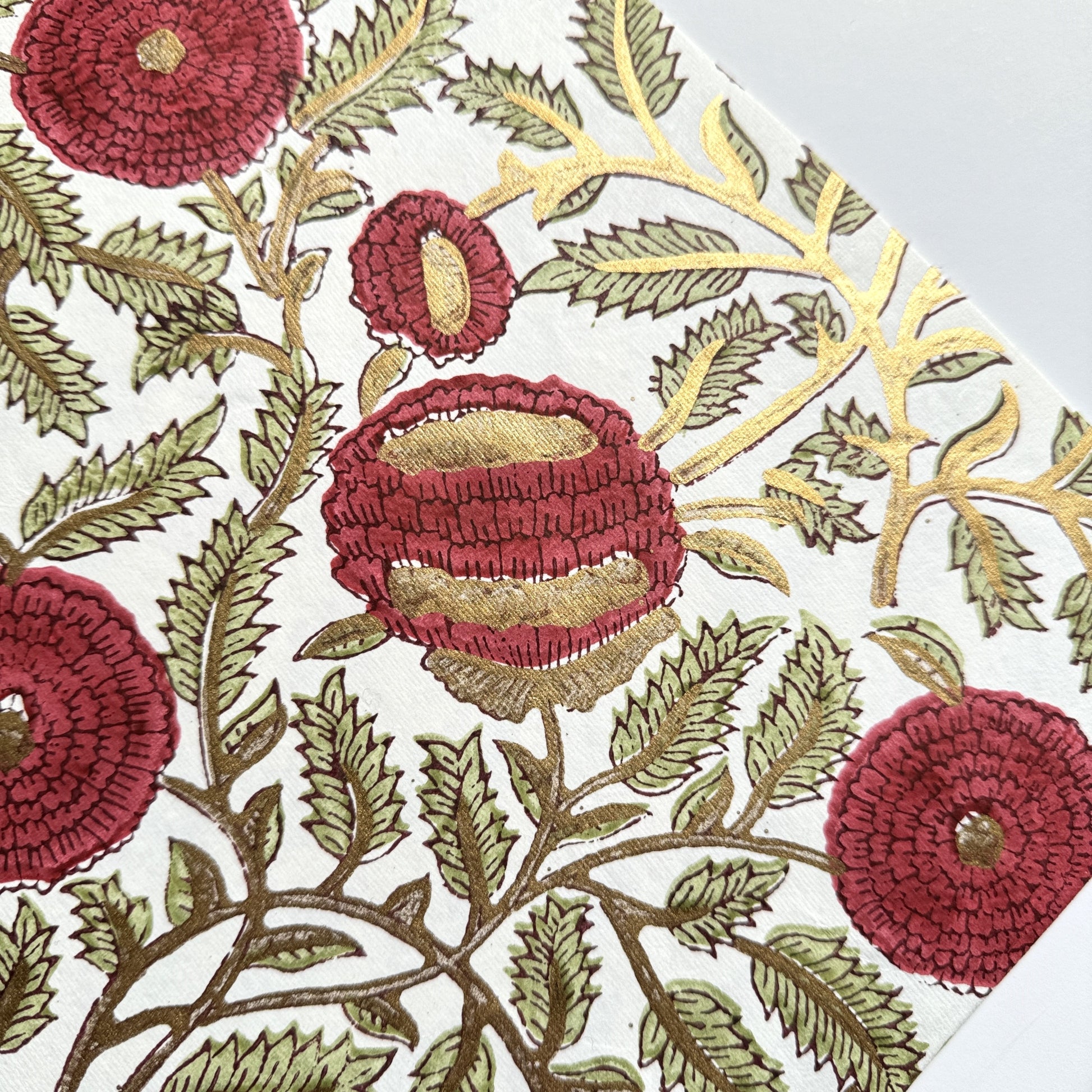 hand block printed paper by Paper Mirchi.  A floral repeat pattern in deep burgundy, pale green and gold. Close up to show the gold in the pattern