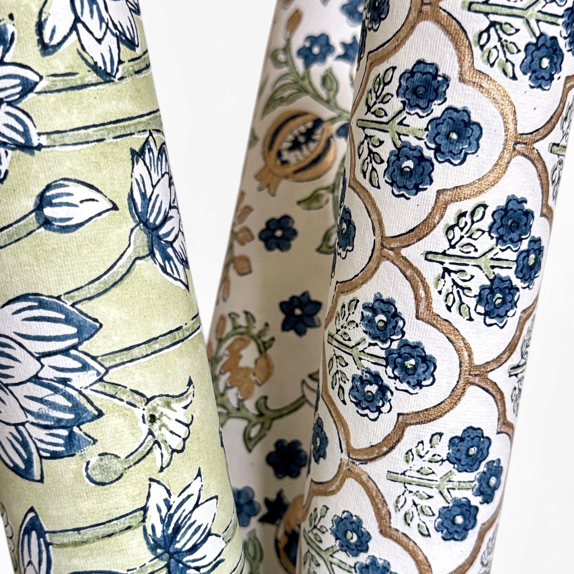 hand block printed wrapping paper with a small flower design in indigo and green surrounded by a gold trellis design. By Paper Mirchi. Rolled, alongside complementing designs