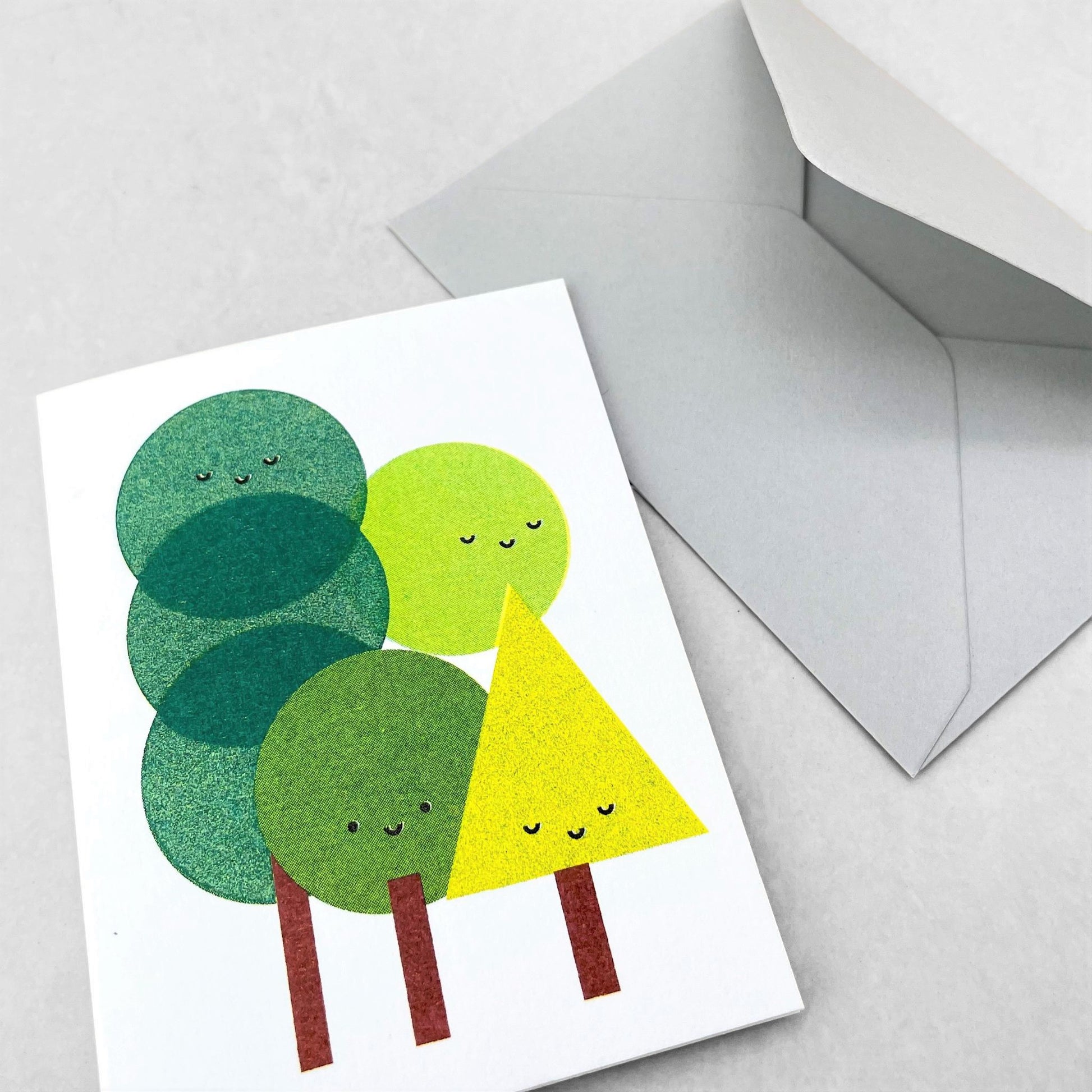 Mini greetings card with an image of a group of trees with smily faces. By Scout Editions.