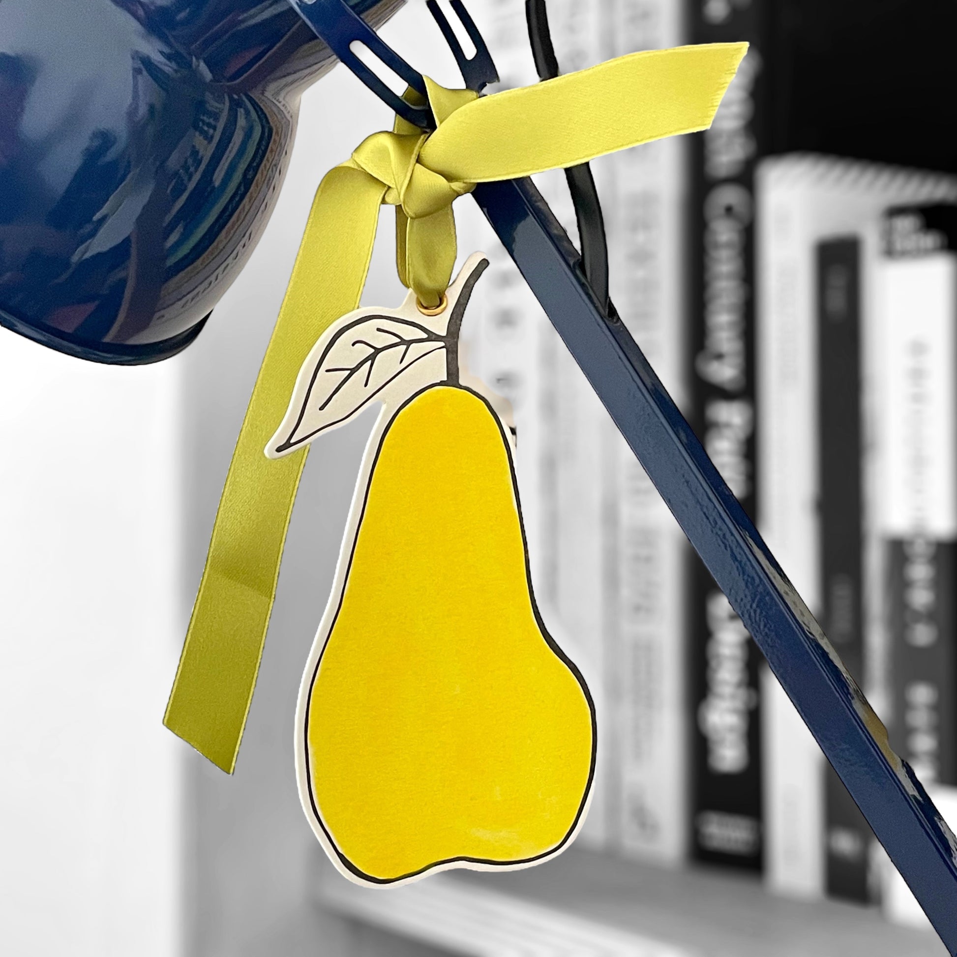 a pear shaped hanging ornament made of thick 1050gsm off-white card, letterpress printed in black and then hand painted in bright yellow ink. It has a chartreuse green satin ribbon to hang the ornament with. By Scribble & Daub, hanging from a lamp