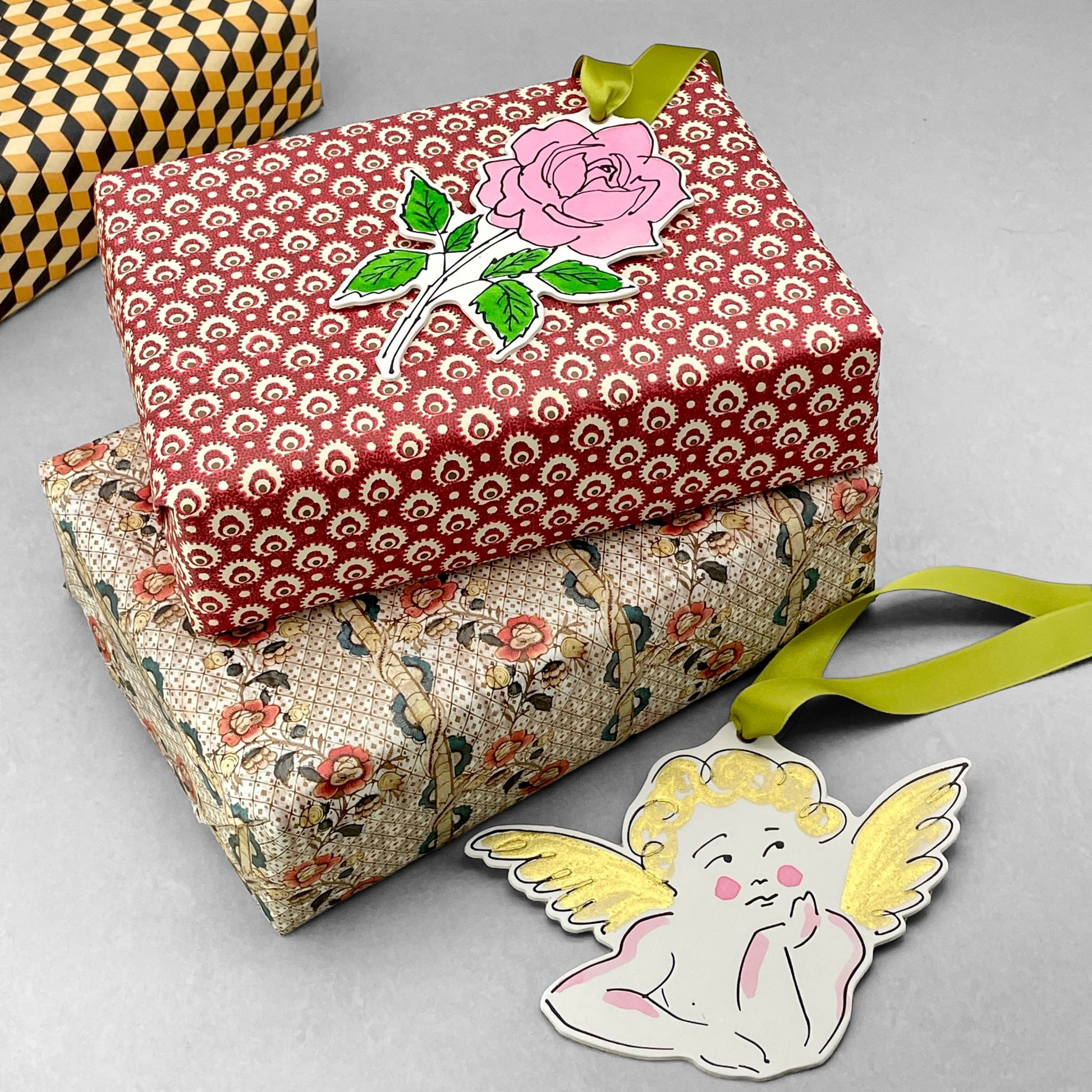 a rose shaped hanging ornament made of thick 1050gsm off-white card, letterpress printed in black and then hand painted in pink and green ink. It has a chartreuse green satin ribbon to hang the ornament with. By Scribble & Daub. Pictured as a gift tag