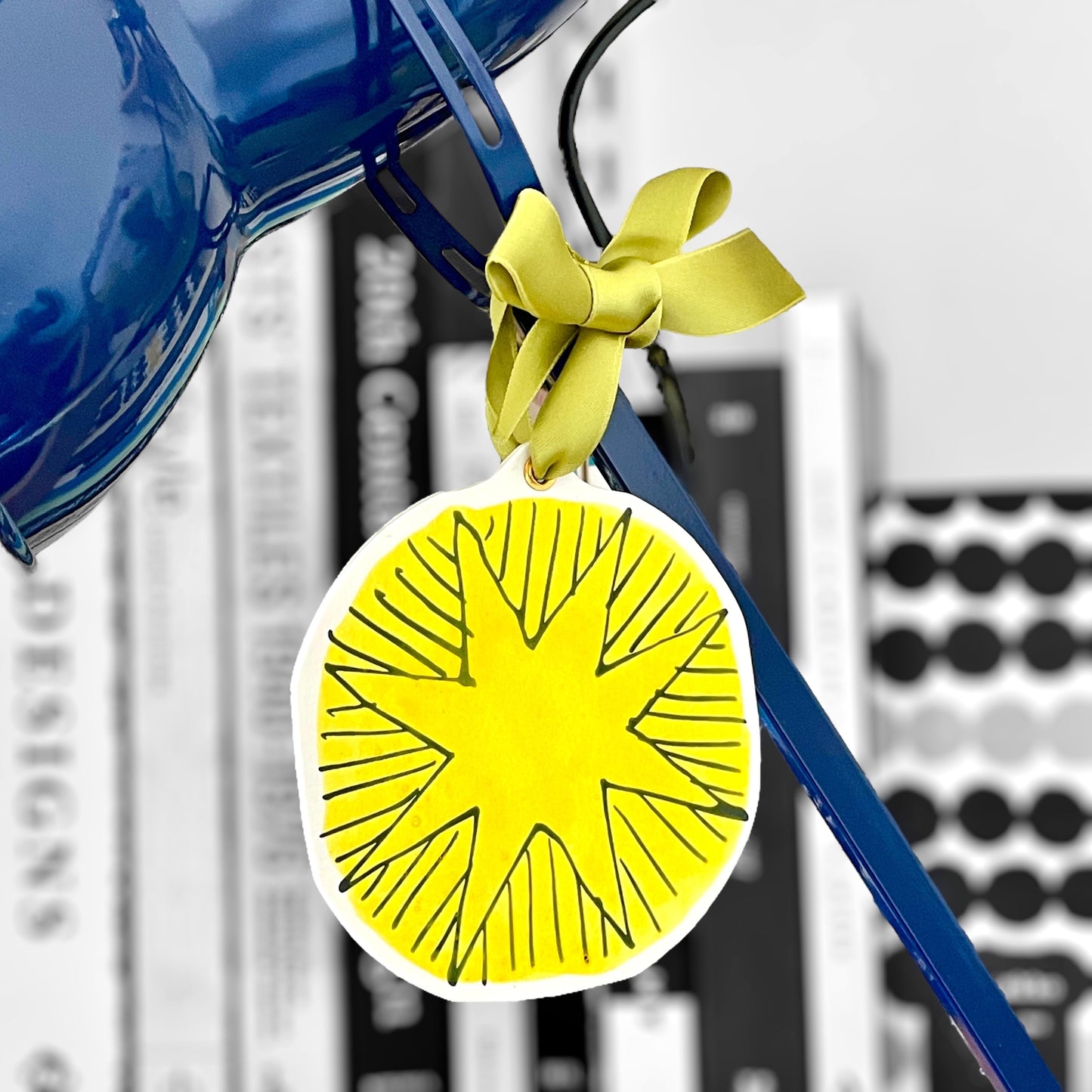 a star shaped hanging ornament made of thick 1050gsm off-white card, letterpress printed in black and then hand painted in yellow ink. It has a chartreuse green satin ribbon to hang the ornament with. By Scribble & Daub. Hanging from a lamp