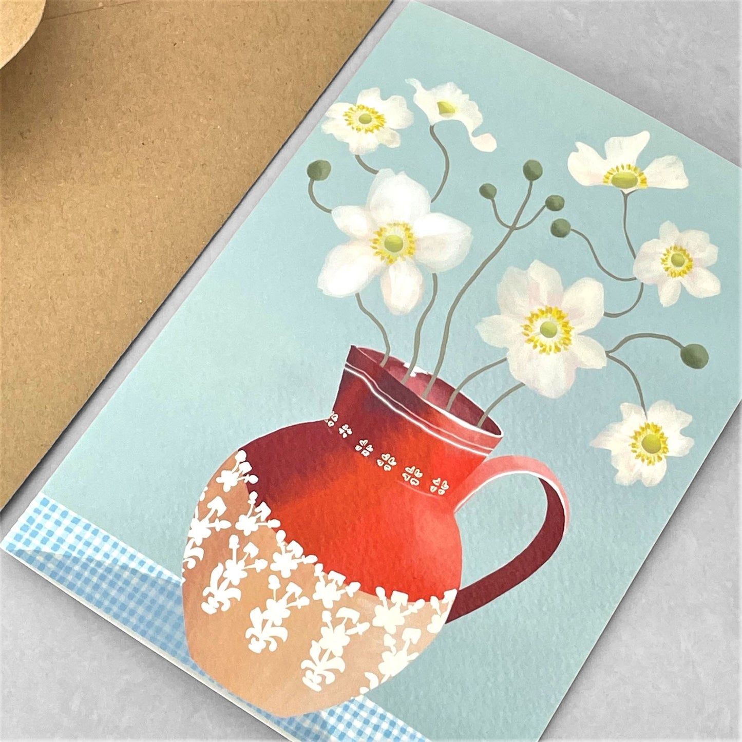 greeting card of a painting of white anemones in in red jug, against a pale blue background by Susie Hamilton