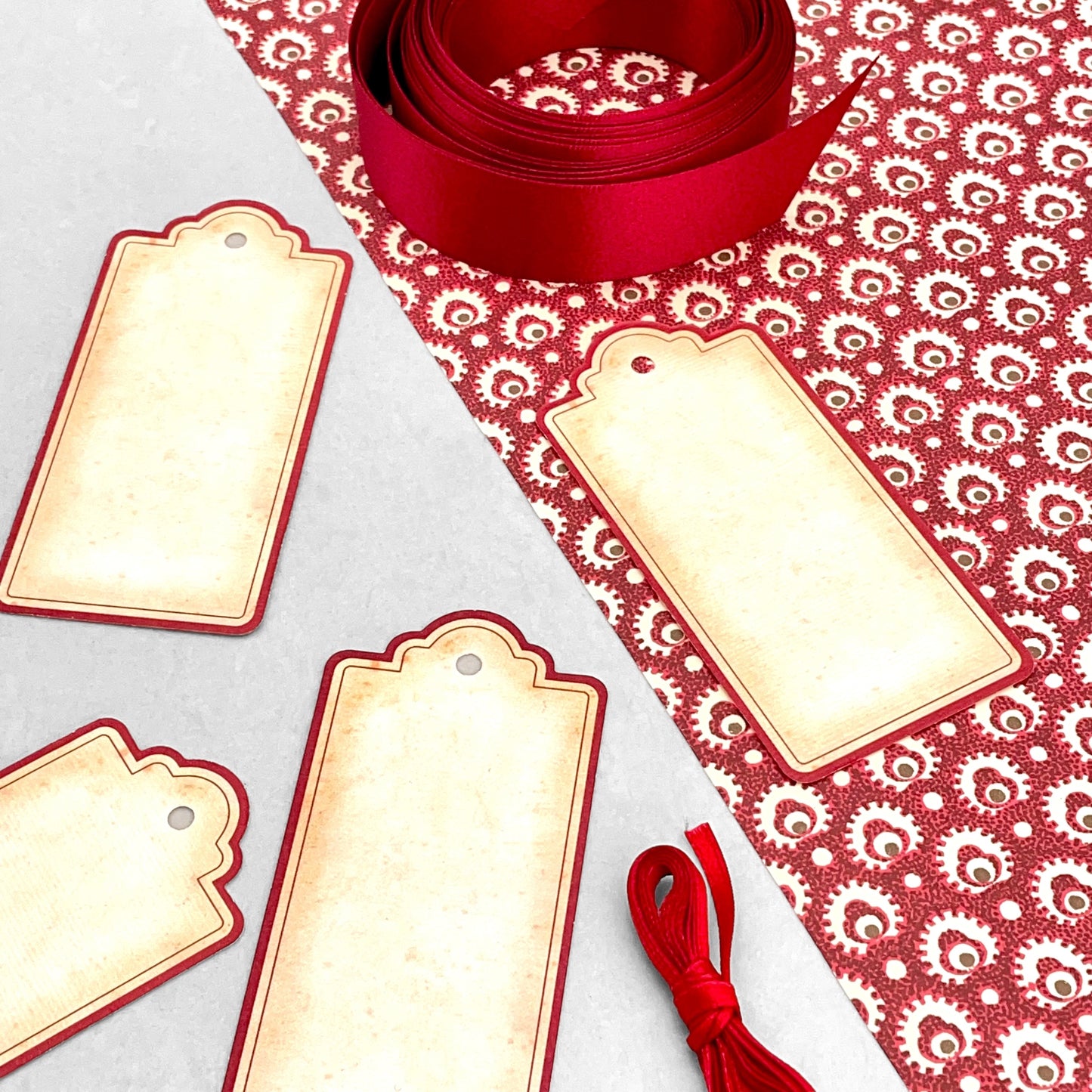 set of 4 vintage style gift tags by Grafiche Tassotti. Rectangular with sepia colour paper and red border. Presented with red ribbon. Pictured with some red Italian wrapping paper