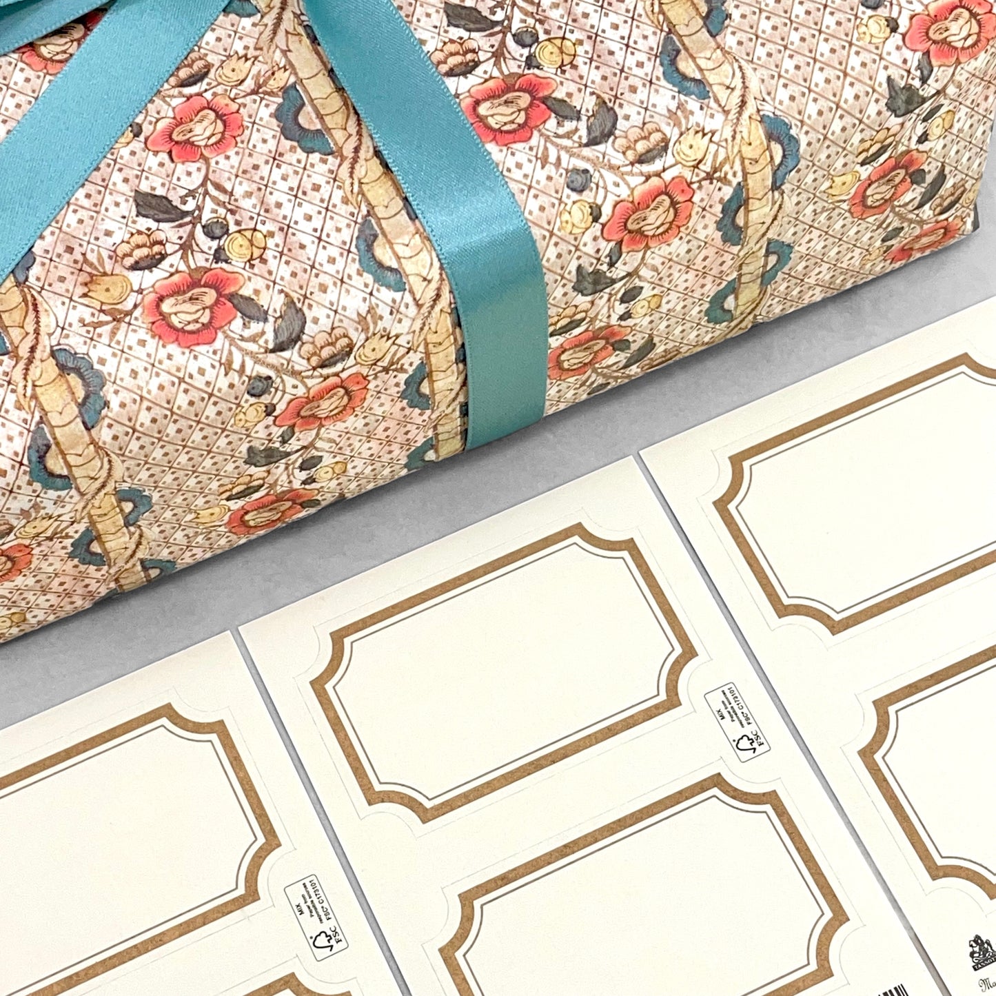 Adhesive labels made of ivory paper with a gold rectangular border by Grafiche Tassotti, Pictured alongside a wrapped present