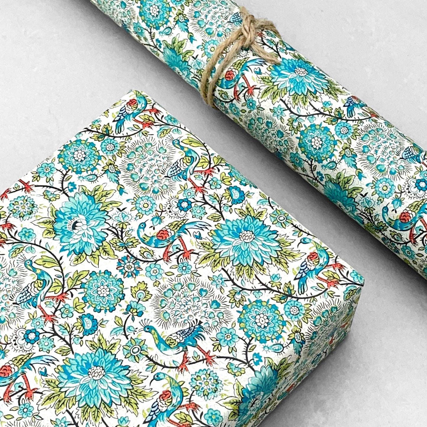 italian patterned wrapping paper "Carta Varese" by Grafiche Tassotti. Pattern of peacocks, flowers and foliage in tones of blue, aqua, green and red.  Pictured as a present