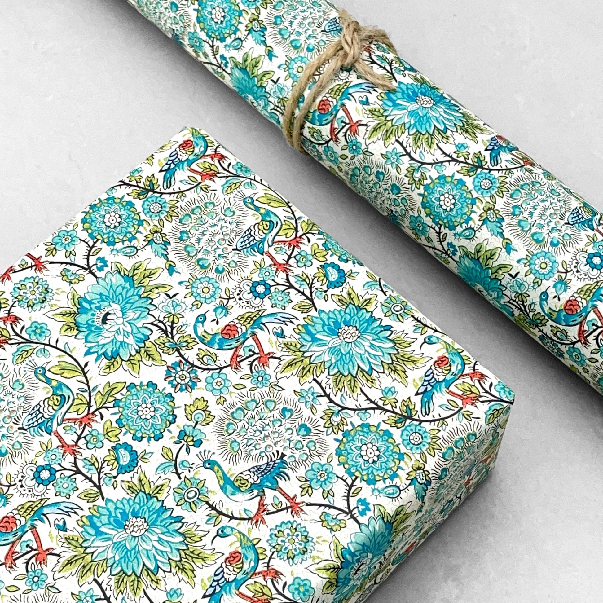 italian patterned wrapping paper "Carta Varese" by Grafiche Tassotti. Pattern of peacocks, flowers and foliage in tones of blue, aqua, green and red.  Pictured as a present