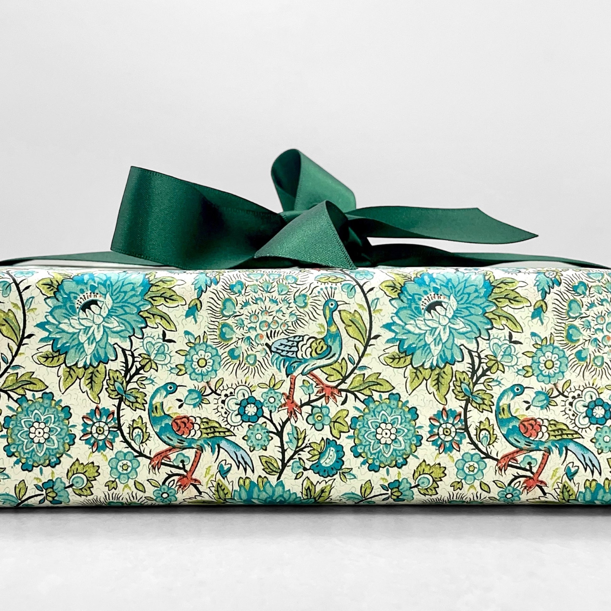 italian patterned wrapping paper "Carta Varese" by Grafiche Tassotti. Pattern of peacocks, flowers and foliage in tones of blue, aqua, green and red. Pictured as a present