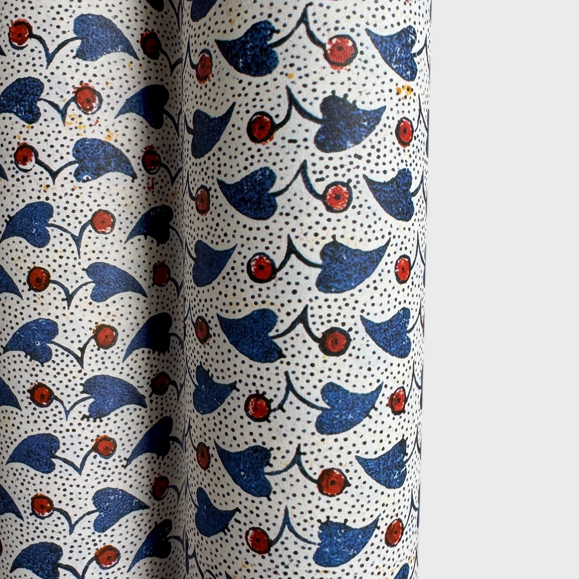 a sheet of italian wrapping paper with a blue little heart shaped leaves and red berries on white background. Close up
