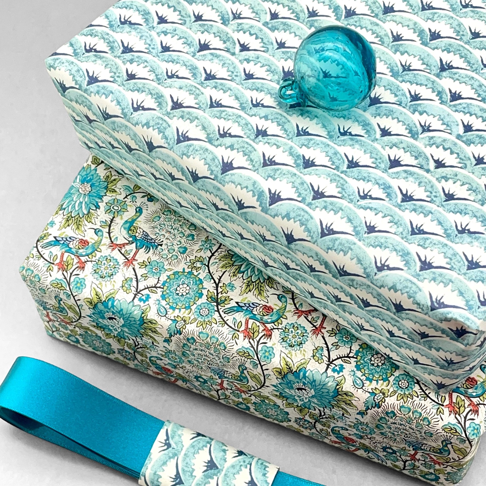 italian Remondini patterned wrapping paper by Tassotti.. All over repeat pattern of block printed style waves in aqua, dark blue on white background.  Pictured wrapped as a present alongside another design